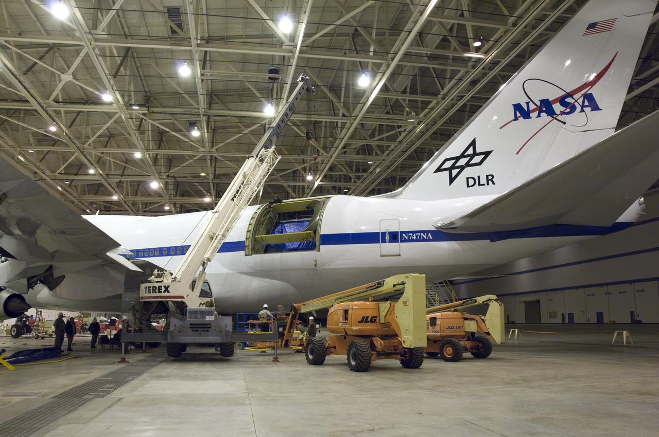 A large mobile crane and hi-lift are maneuvered into place for removal of the aperture assembly and cavity doors from NASA's SOFIA observatory aircraft.