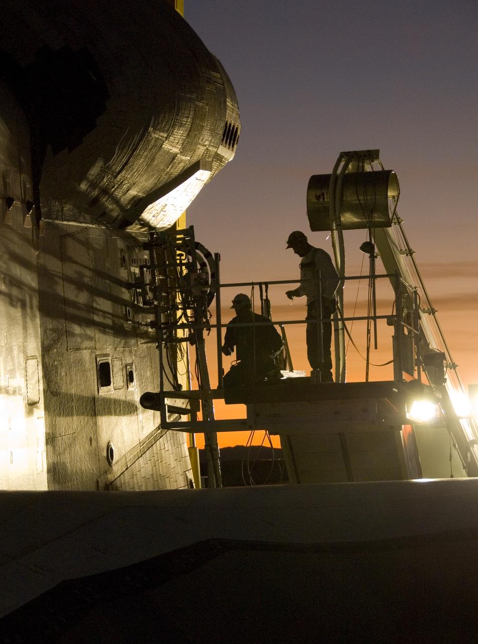 As dusk settles over Edwards Air Force Base, NASA technicians hook up various ground-support systems before shuttle Endeavour is towed off the landing runway.