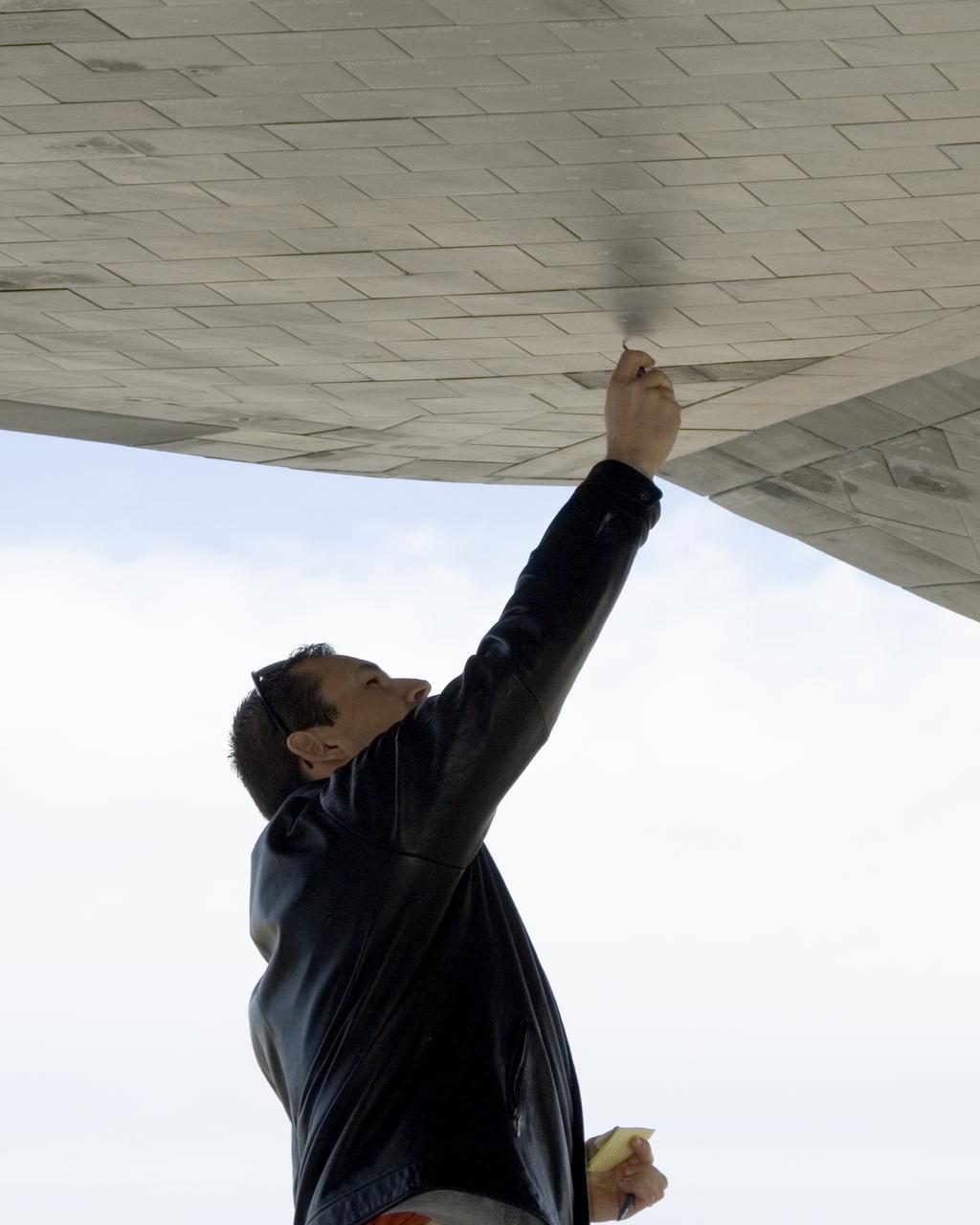 A United Space Alliance technician carefully checks the thermal tiles on the underside of Space Shuttle Endeavour for nicks and dings following its landing at Edwards Air Force Base to conclude mission STS-126.