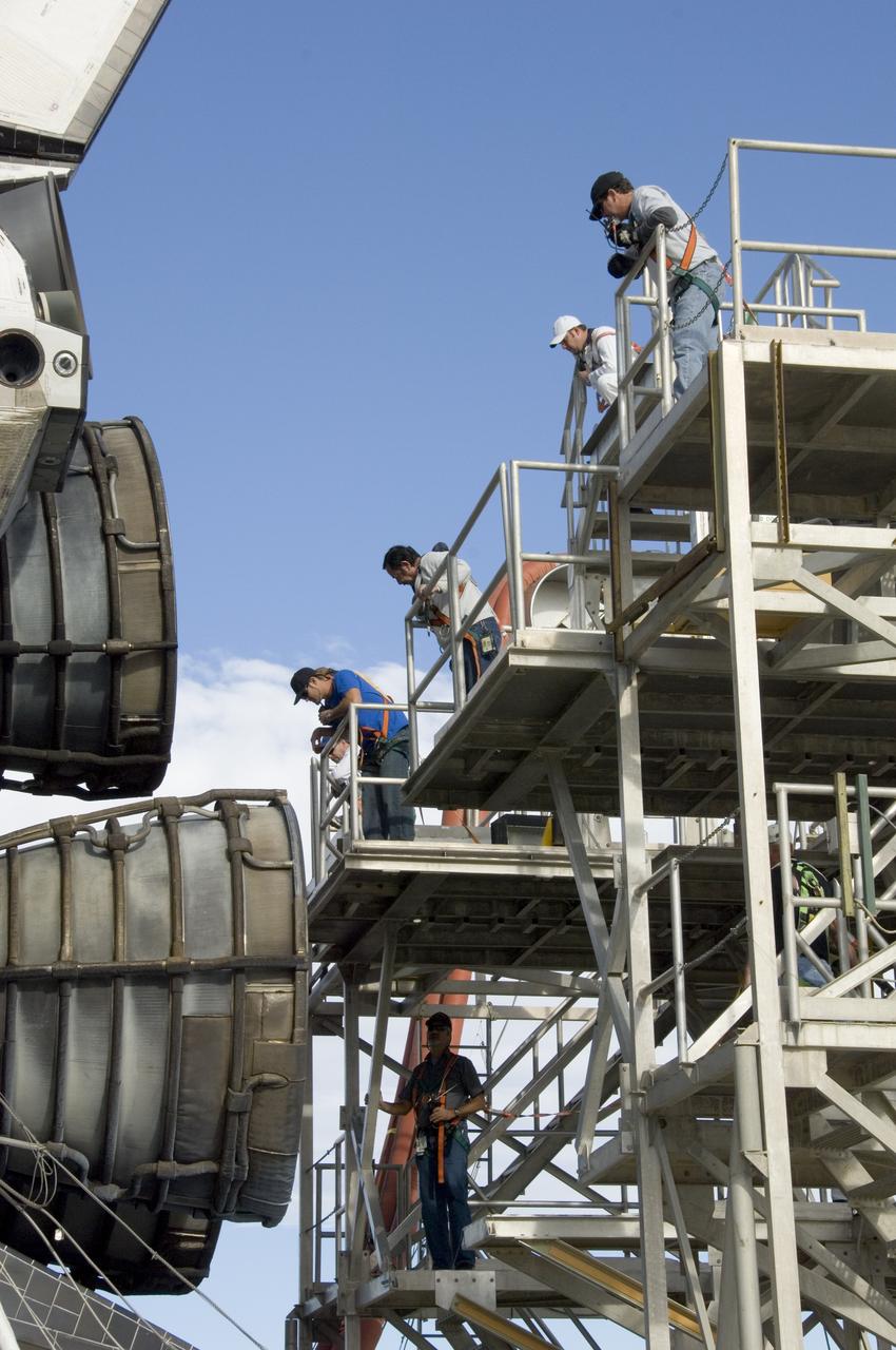 Technicians monitor the positioning of a large workstand as it is carefully moved into place around the main engine nozzles of Space Shuttle Endeavour during deservicing and ferry flight preparations at NASA's Dryden Flight Research Center at Edwards Air Force Base.