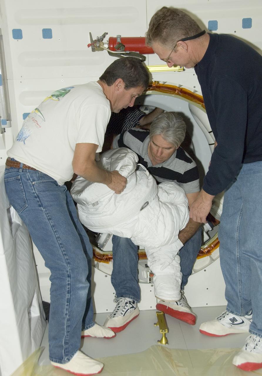 United Space Alliance flight systems technicians Troy Mann, Mark Shimei and Jim Smodell remove the lower portion of an Extravehicular Mobility Unit (EMU) suit from Endeavour's airlock.