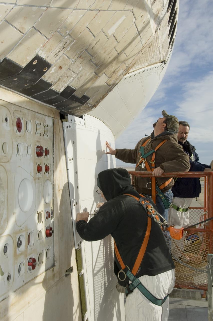 Technicians fasten down the flanges of the aerodynamic tail cone after installation on NASA's Space Shuttle Endeavour prior to its ferry flight from NASA's Dryden Flight Research Center to NASA's Kennedy Space Center in Florida.