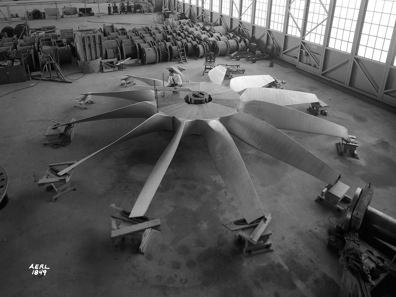 National Advisory Committee for Aeronautics (NACA) engineers assembled the Altitude Wind Tunnel’s (AWT) large wooden drive fan inside the hangar at the Aircraft Engine Research Laboratory. When it was built at the in the early 1940s the AWT was among the most complex test facilities ever designed. It was the first wind tunnel capable of operating full-scale engines under realistic flight conditions. This simulation included the reduction of air temperature, a decrease in air pressure, and the creation of an airstream velocity of up to 500 miles per hour. The AWT was constructed in 1942 and 1943. This photograph shows NACA engineers Lou Hermann and Jack Aust assembling the tunnel’s drive fan inside the hangar. The 12-bladed, 31-foot-diameter spruce wood fan would soon be installed inside the wind tunnel to create the high-speed airflow. This massive propeller was designed and constructed by the engine lab's design team at Langley Field. John Breisch, a Langley technician with several years of wind tunnel installation experience, arrived in Cleveland at the time of this photograph to supervise the fan assembly inside the hangar. He would return several weeks later to oversee the actual installation in the tunnel. The fan was driven at 410 revolutions per minute by an 18,000-horsepower General Electric induction motor that was located in the rear corner of the Exhauster Building. An extension shaft connected the motor to the fan. A bronze screen protected the fan against damage from failed engine parts sailing through the tunnel. Despite this screen the blades did become worn or cracked over time and had to be replaced. An entire new fan was installed in 1951.