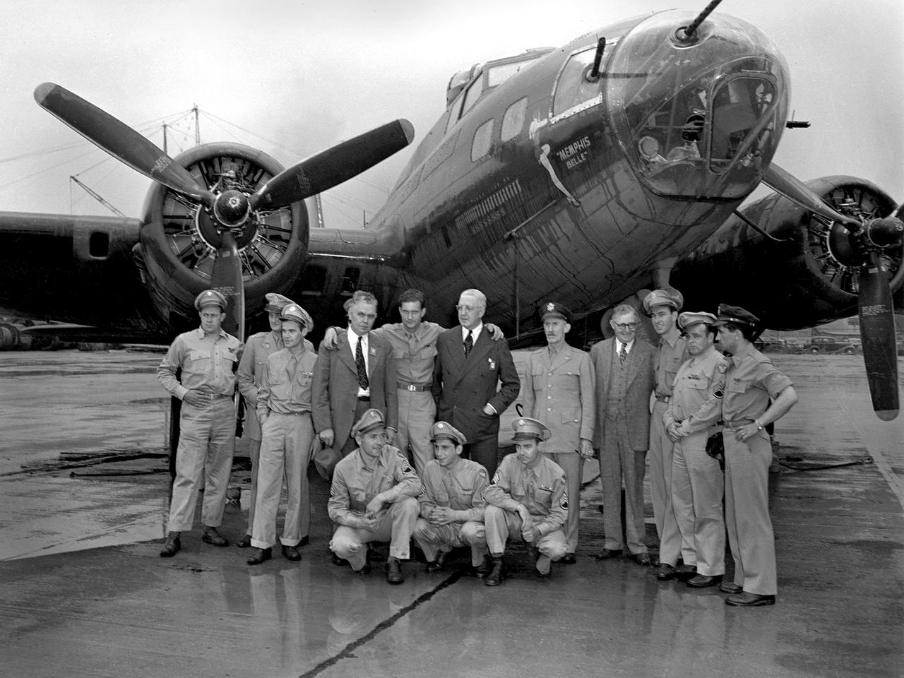 Captain Robert Morgan and the rest of the Memphis Belle crew arrive in Cleveland on a rainy July 7, 1943, for three-day publicity visit. This B–17 Flying Fortress had recently become the first U.S. bomber to complete 25 missions over Germany and France. The lack of long distance escort fighters made the feat even more remarkable. The Memphis Belle and its crew returned to the United States in June and were immediately thrown into a three-month-long war bond tour.  While in Cleveland the crew toured the National Advisory Committee for Aeronautics (NACA) Aircraft Engine Research Laboratory, the Cleveland Bomber Plant, and Thompson Products. In the evenings they were feted downtown by the Chamber of Commerce at the Hotel Cleveland. A local company brought Morgan’s family and his fiancé—the Memphis Belle’s inspiration—to Cleveland to participate in the activities. The bomber was on display to the public near the airport’s fenceline and stored in the NACA’s hangar overnight.    Pictured in this photograph from left to right: Robert Hanson, Vincent Evans, Charles Leighton, NACA Manager Raymond Sharp, Robert Morgan, William Holliday of the Chamber of Commerce, Army Liaison Officer Colonel Edwin Page, Airport Commissioner Jack Berry, Cecil Scott, John Quinlan and James Verinis. Kneeling are Harold Loch, Casimer Nastal and Charles Wichell.