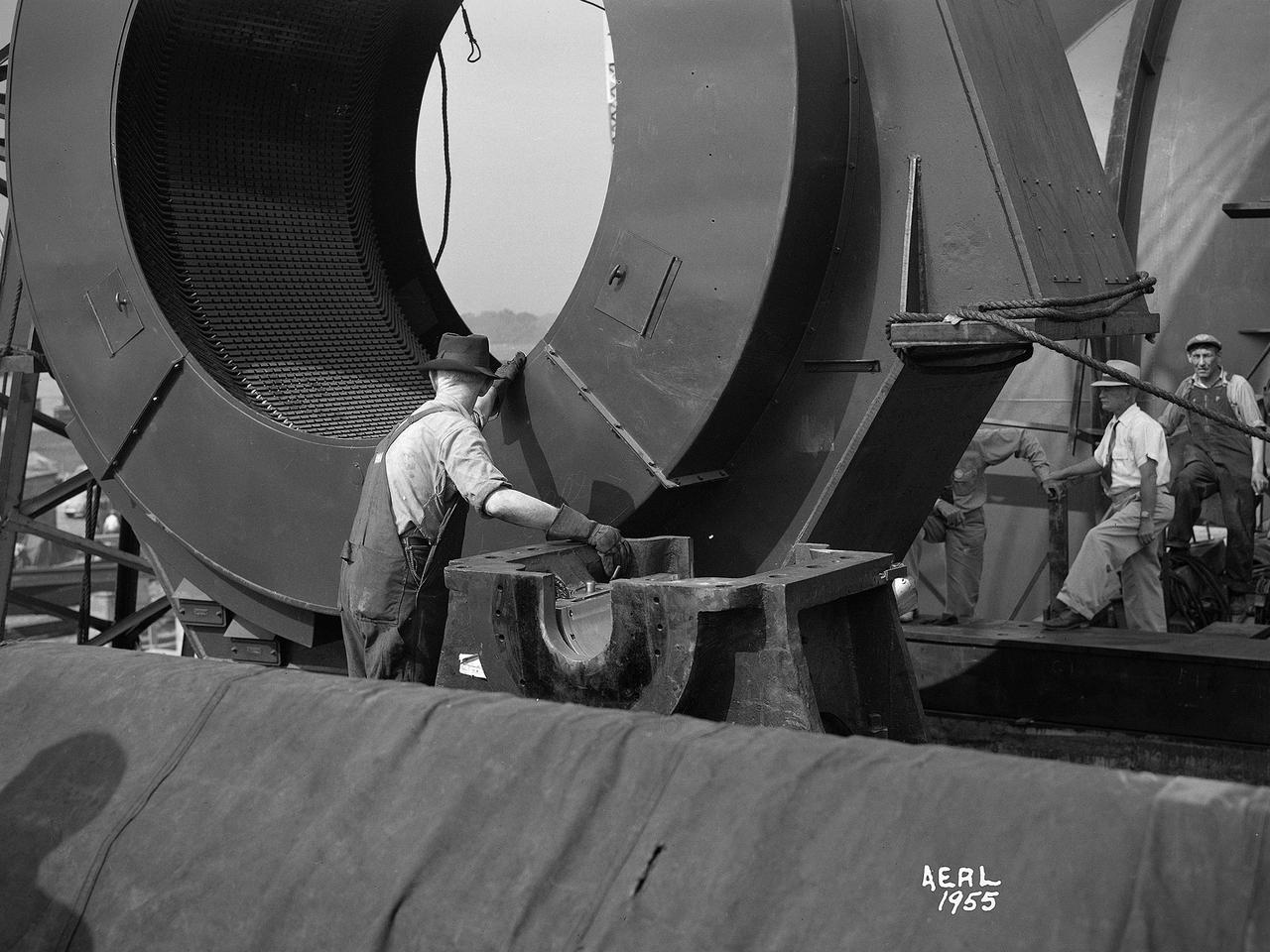 Construction workers install the drive motor for the Altitude Wind Tunnel (AWT) in the Exhauster Building at the National Advisory Committee for Aeronautics (NACA) Aircraft Engine Research Laboratory. The AWT was capable of operating full-scale engines in air density, speed, and temperature similar to that found at high altitudes. The tunnel could produce wind speeds up to 500 miles per hour through a 20-foot-diameter test section at the standard operating altitude of 30,000 feet. The airflow was created by a large wooden fan near the tunnel’s southeast corner.       This photograph shows the installation of the 18,000-horsepower drive motor inside the adjoining Exhauster Building in July 1943. The General Electric motor, whose support frame is seen in this photograph, connected to a drive shaft that extended from the building, through the tunnel shell, and into a 12-bladed, 31-foot-diameter spruce wood fan. Flexible couplings on the shaft allowed for the movement of the shell. The corner of the Exhauster Building was built around the motor after its installation.    The General Electric induction motor could produce 10 to 410 revolutions per minute and create wind speeds up to 500 miles per hour, or Mach 0.63, at 30,000 feet. The AWT became operational in January 1944 and tested piston, turbojet and ramjet engines for nearly 20 years.