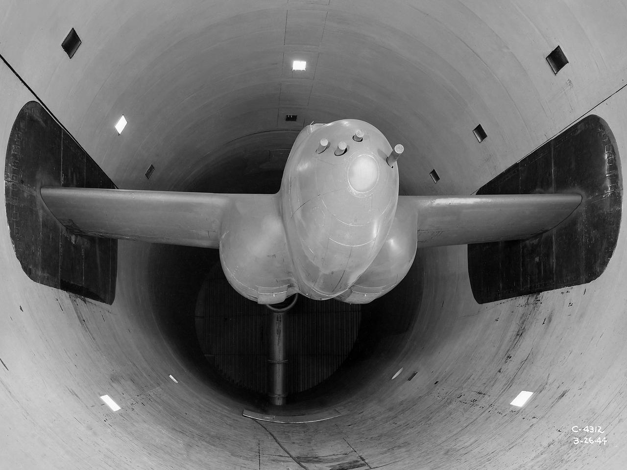 The Altitude Wind Tunnel (AWT) was the National Advisory Committee for Aeronautics (NACA) Aircraft Engine Research Laboratory’s largest and most important test facility in the 1940s. The AWT employed massive cooling and exhaust systems to simulate conditions found at high altitudes. The facility was originally designed to test large piston engines in a simulated flight environment. The introduction of the turbojet during the tunnel’s construction, however, changed the facility’s focus before it became operational. Its first test program was a study of the Bell YP–59A Airacomet and its General Electric I–16 turbojets.       The Airacomet was the United States’ first attempt to build a jet aircraft.  1600-horsepower centrifugal engines based on an early design by British engineer Frank Whittle were incorporated into an existing Bell airframe. In October 1942 the Airacomet was secretly test flown in the California desert. The aircraft’s performance was limited, however, and the NACA was asked to study the engines in the AWT.    The wind tunnel’s 20-foot-diameter test section was large enough to accommodate entire aircraft with its wing tips and tail removed. The I-16 engines were studied exhaustively in early 1944. They first analyzed the engines in their original configuration and then implemented a boundary layer removal duct, a new nacelle inlet, and new cooling seals. Tests of the modified version showed that the improved distribution of airflow increased the I–16’s performance by 25 percent. The Airacomet never overcame some of its inherent design issues, but the AWT went on to study nearly every emerging US turbojet model during the next decade.