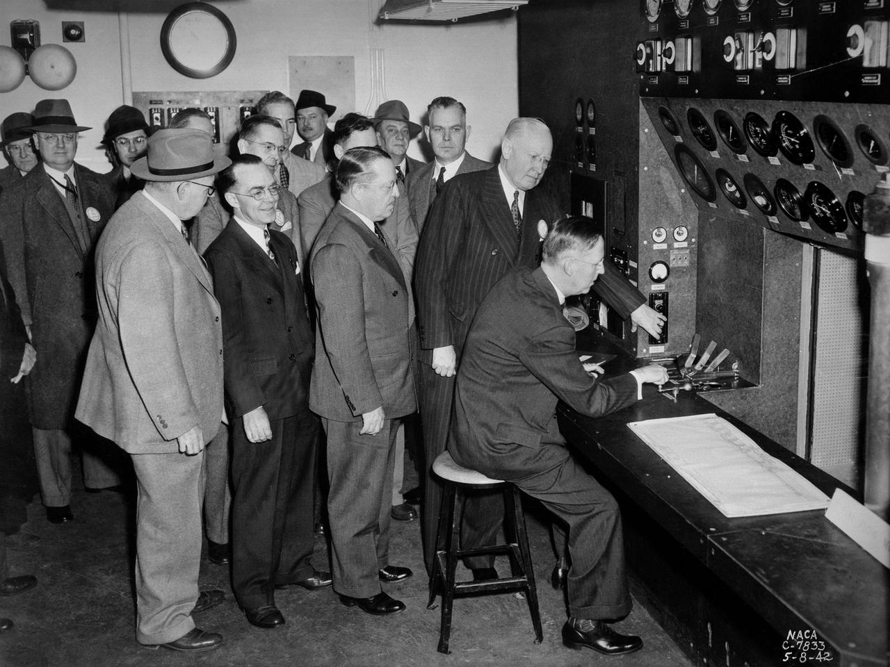 A group of National Advisory Committee for Aeronautics (NACA) officials and local dignitaries were on hand on May 8, 1942, to witness the Initiation of Research at the NACA's new Aircraft Engine Research Laboratory in Cleveland, Ohio. The group in this photograph was in the control room of the laboratory's first test facility, the Engine Propeller Research Building. The NACA press release that day noted, "First actual research activities in what is to be the largest aircraft engine research laboratory in the world was begun today at the National Advisory Committee for Aeronautics laboratory at the Cleveland Municipal Airport.” The ceremony, however, was largely symbolic since most of the laboratory was still under construction.     Dr. George W. Lewis, the NACA's Director of Aeronautical Research, and John F. Victory, NACA Secretary, are at the controls in this photograph. Airport Manager John Berry, former City Manager William Hopkins, NACA Assistant Secretary Ed Chamberlain, Langley Engineer-in-Charge Henry Reid, Executive Engineer Carlton Kemper, and Construction Manager Raymond Sharp are also present.    The propeller building contained two torque stands to test complete engines at ambient conditions. The facility was primarily used at the time to study engine lubrication and cooling systems for World War II aircraft, which were required to perform at higher altitudes and longer ranges than previous generations.