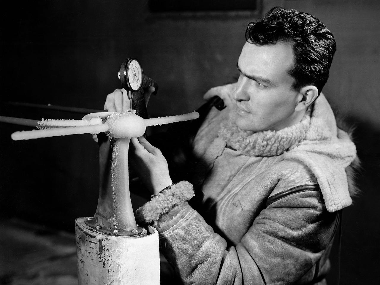 A National Advisory Committee for Aeronautics (NACA) researcher measures the ice thickness on a landing antenna model in the Icing Research Tunnel at the Aircraft Engine Research Laboratory. NACA design engineers added the Icing Research Tunnel to the original layout of the new Aircraft Engine Research Laboratory to take advantage of the massive refrigeration system being built for the Altitude Wind Tunnel. The Icing Research Tunnel was built to study the formation of ice on aircraft surfaces and methods of preventing or eradicating that ice. Ice buildup adds extra weight, effects aerodynamics, and sometimes blocks air flow through engines.       The Icing Research Tunnel is a closed-loop atmospheric wind tunnel with a 6- by 9-foot test section. Carrier Corporation refrigeration equipment reduced the internal air temperature to -45 degrees F and a spray bar system injected water droplets into the air stream. The 24-foot diameter drive fan, seen in this photograph, created air flows velocities up to 400 miles per hour.    The Icing Research Tunnel began testing in June of 1944. Early testing, seen in this photograph, studied ice accumulation on propellers and antenna of a military aircraft. The Icing Research Tunnel’s designers, however, struggled to develop a realistic spray system since they did not have access to data on the size of naturally occurring water droplets. The system would have to generate small droplets, distribute them uniformly throughout the airstream, and resist freezing and blockage. For five years a variety of different designs were painstakingly developed and tested before the system was perfected.