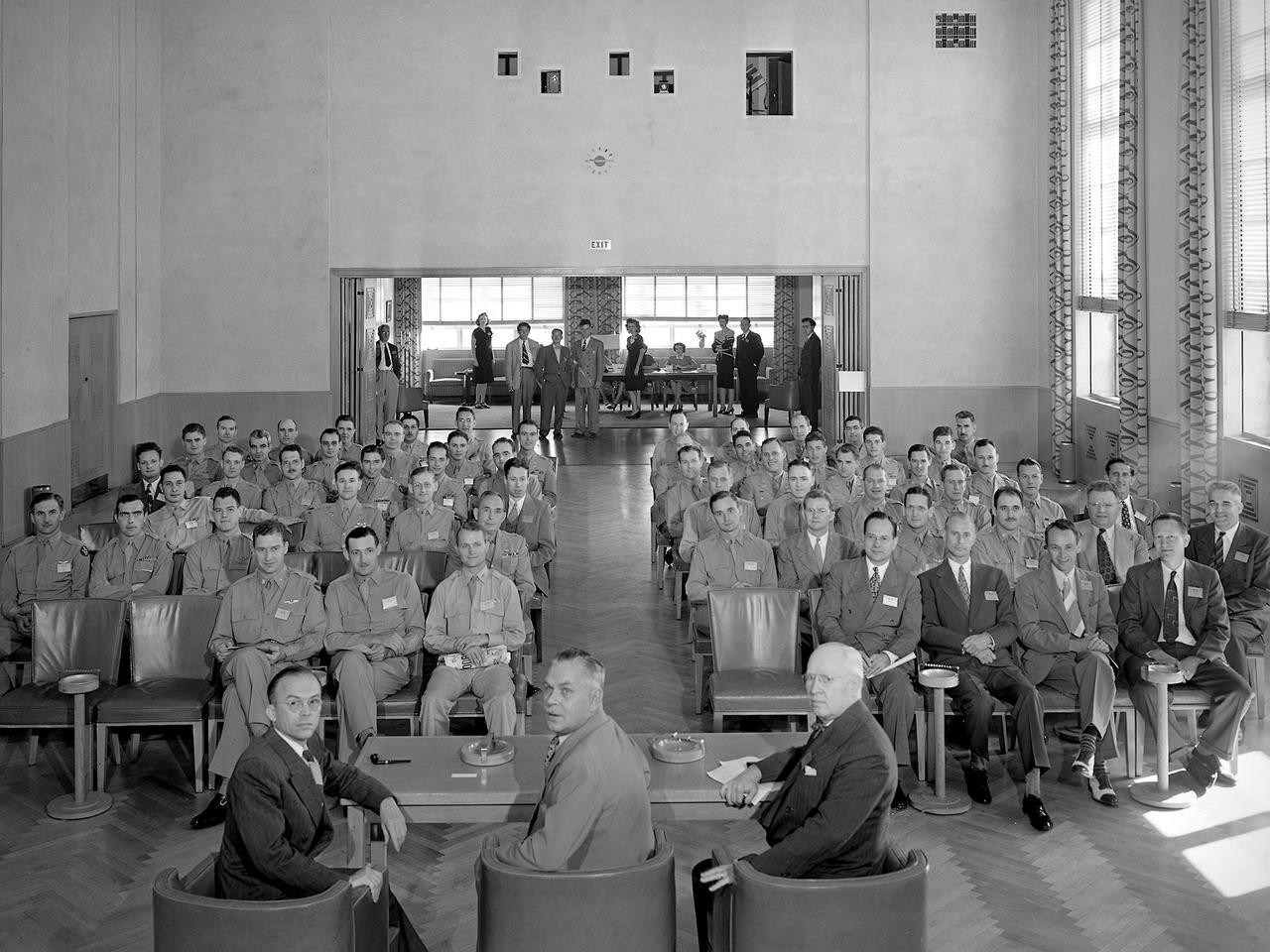 A group of 60 Army Air Forces officers visited the National Advisory Committee for Aeronautics (NACA) Aircraft Engine Research Laboratory on August 27, 1945. The laboratory enacted strict security regulations throughout World War II. During the final months of the war, however, the NACA began opening its doors to groups of writers, servicemen, and aviation industry leaders. These events were the first exposure of the new engine laboratory to the outside world. Grandstands were built alongside the Altitude Wind Tunnel specifically for group photographs.    George Lewis, Raymond Sharp, and Addison Rothrock (right to left) addressed this group of officers in the Administration Building auditorium. Lewis was the NACA’s Director of Aeronautical Research, Sharp was the lab’s manager, and Rothrock was the lab’s chief of research. Abe Silverstein, Jesse Hall and others watch from the rear of the room. The group toured several facilities after the talks, including the Altitude Wind Tunnel and a new small supersonic wind tunnel. The visit concluded with a NACA versus Army baseball game and cookout.
