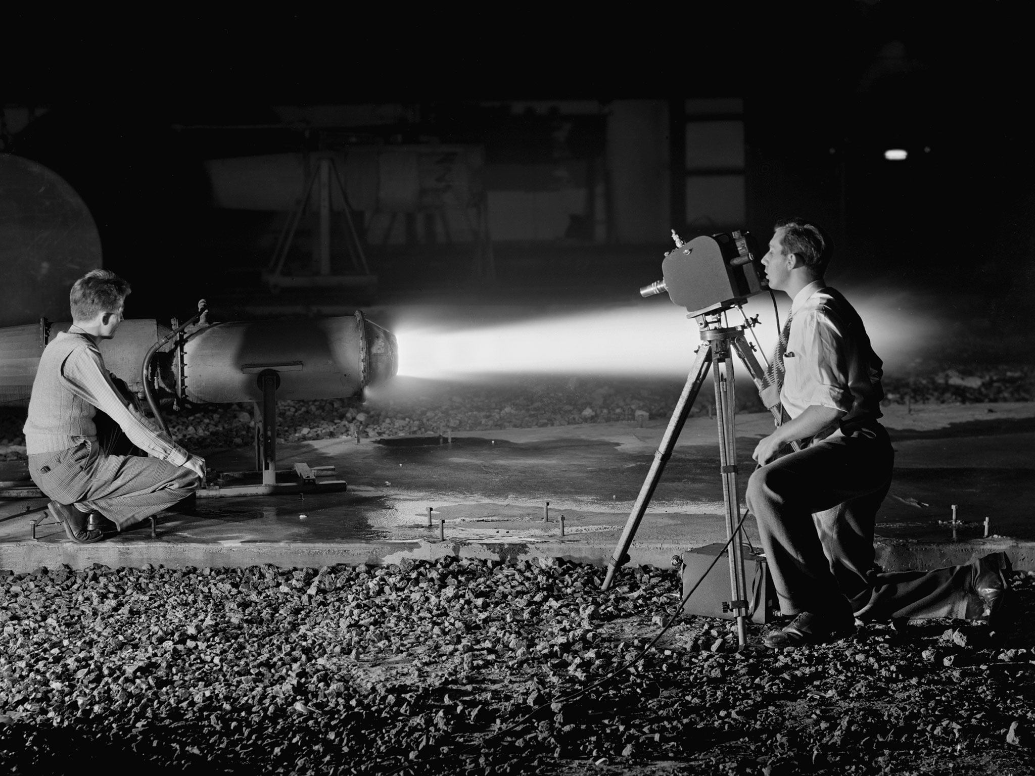 Kneeling photographer films ramjet engine firing at night.
