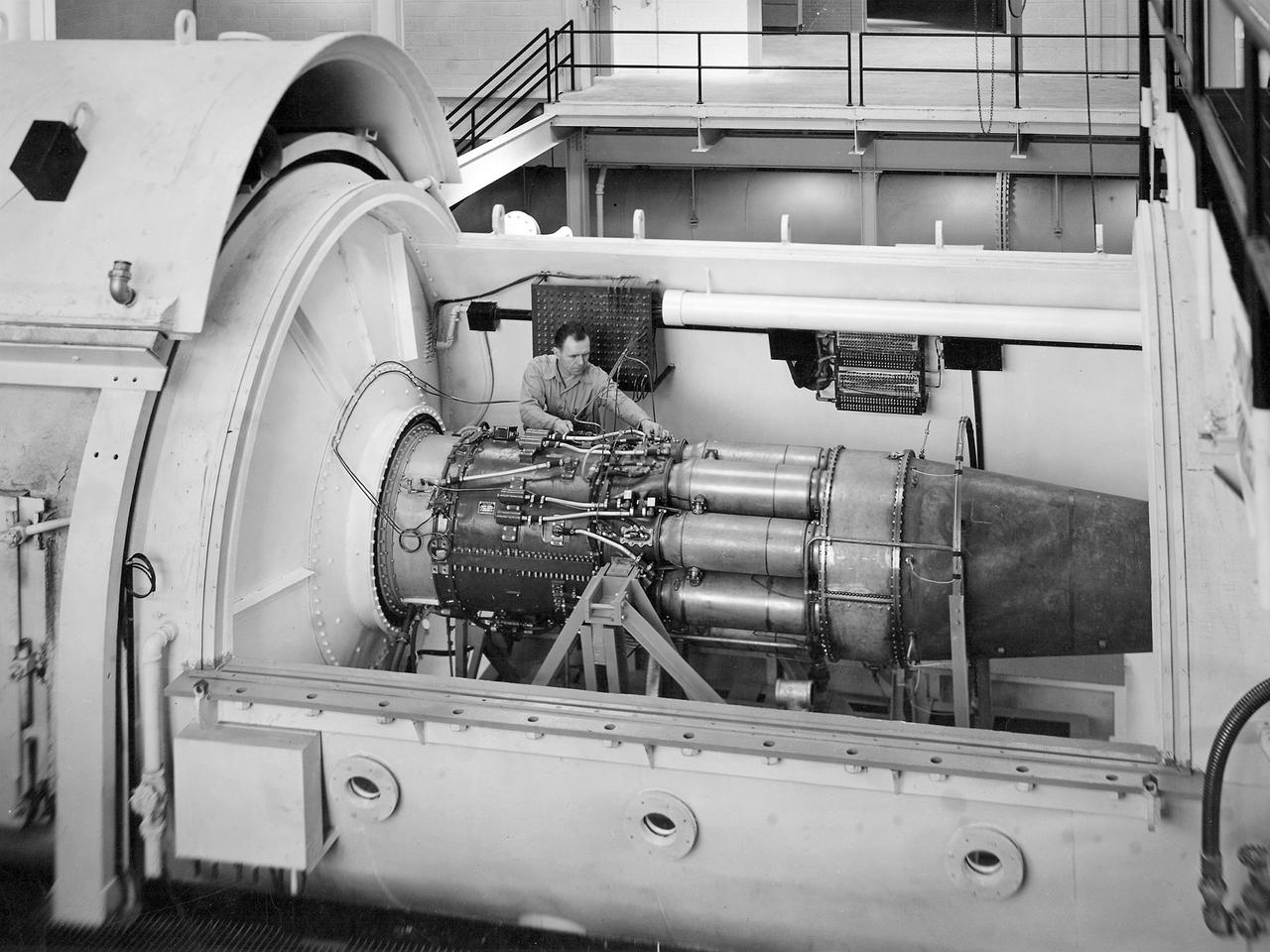 One of the two altitude simulating-test chambers in Engine Research Building at the National Advisory Committee for Aeronautics (NACA) Lewis Flight Propulsion Laboratory. The two chambers were collectively referred to as the Four Burner Area. NACA Lewis’ Altitude Wind Tunnel was the nation’s first major facility used for testing full-scale engines in conditions that realistically simulated actual flight. The wind tunnel was such a success in the mid-1940s that there was a backlog of engines waiting to be tested. The Four Burner chambers were quickly built in 1946 and 1947 to ease the Altitude Wind Tunnel’s congested schedule.    The Four Burner Area was located in the southwest wing of the massive Engine Research Building, across the road from the Altitude Wind Tunnel. The two chambers were 10 feet in diameter and 60 feet long. The refrigeration equipment produced the temperatures and the exhauster equipment created the low pressures present at altitudes up to 60,000 feet.    In 1947 the Rolls Royce Nene was the first engine tested in the new facility. The mechanic in this photograph is installing a General Electric J-35 engine. Over the next ten years, a variety of studies were conducted using the General Electric J-47 and Wright Aeronautical J-65 turbojets. The two test cells were occasionally used for rocket engines between 1957 and 1959, but other facilities were better suited to the rocket engine testing. The Four Burner Area was shutdown in 1959. After years of inactivity, the facility was removed from the Engine Research Building in late 1973 in order to create the High Temperature and Pressure Combustor Test Facility.