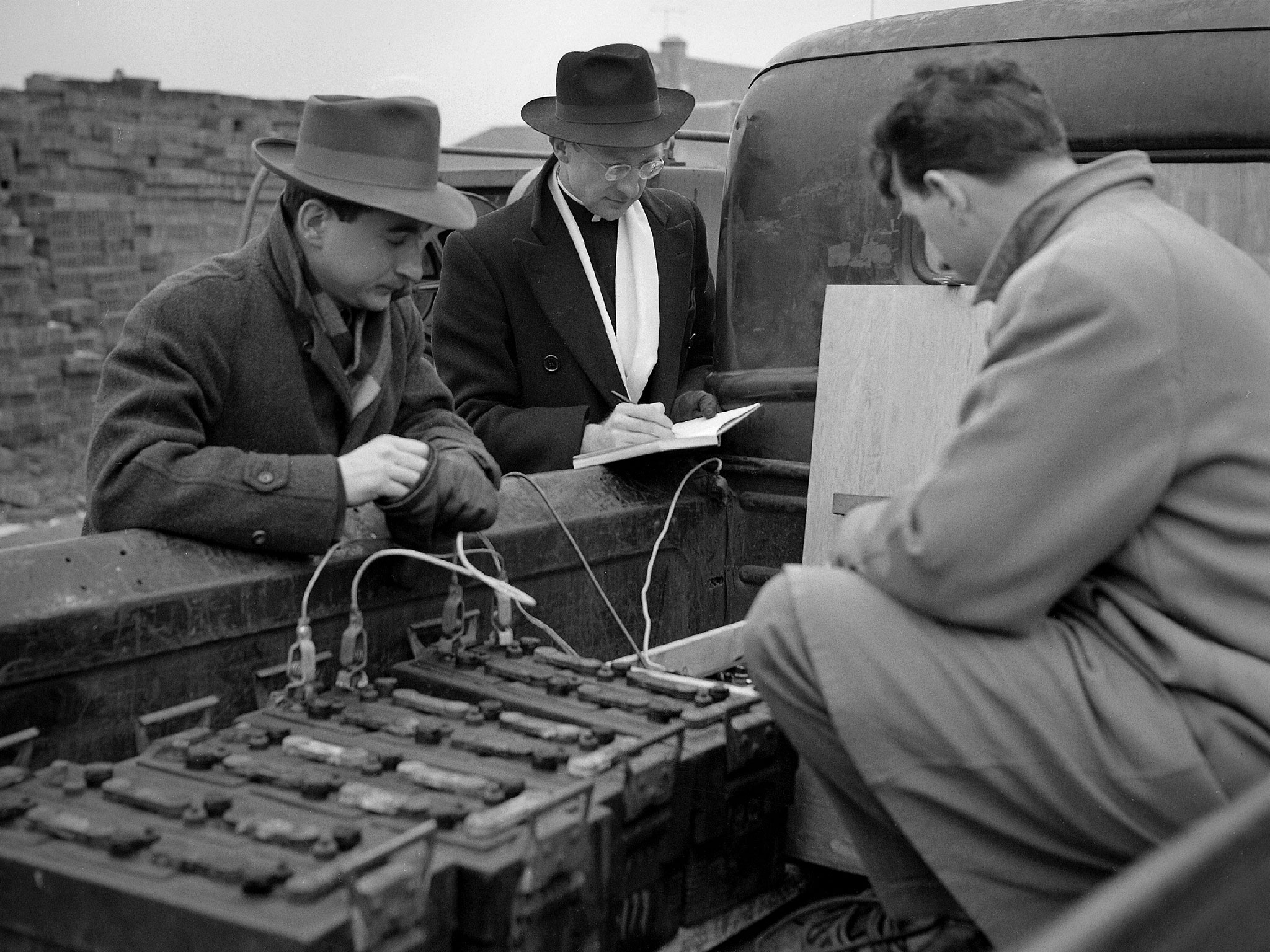 Three men bend over instruments in the back of a truck