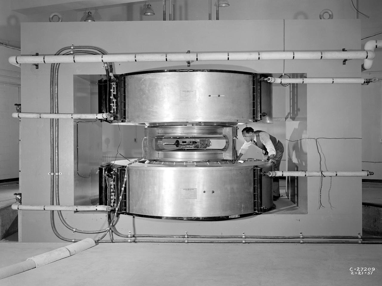 Researcher James Blue examines the new cyclotron at the National Advisory Committee for Aeronautics (NACA) Lewis Flight Propulsion Laboratory. Researchers at NACA Lewis began postulating about the use of atomic power for propulsion immediately after World War II. The NACA concentrated its efforts on the study of high temperature materials and heat transfer since it did not have access to the top secret fission information. The military studied the plausibility of nuclear propulsion for aircraft in the late 1940s. The military program was cancelled after four years without any breakthroughs, but the Atomic Energy Commission took on the effort in 1951. The NACA Lewis laboratory was expanding its nuclear-related research during this period. In 1948, Lewis engineers were assigned to the Oak Ridge National Laboratory to obtain expertise in high temperature heat transfer and advanced materials technology. The following year a new 80-person Nuclear Reactor Division was created, and an in-house nuclear school was established to train these researchers. The cyclotron was built behind the Materials and Structures Laboratory to support thermodynamic and materials research for both nuclear aircraft and nuclear rockets. The original NACA Lewis cyclotron was used to accelerate two kinds of particles. To better match the space radiation environment, the cyclotron was later modified to accelerate particles of the newly-discovered Van Allen radiation belts.