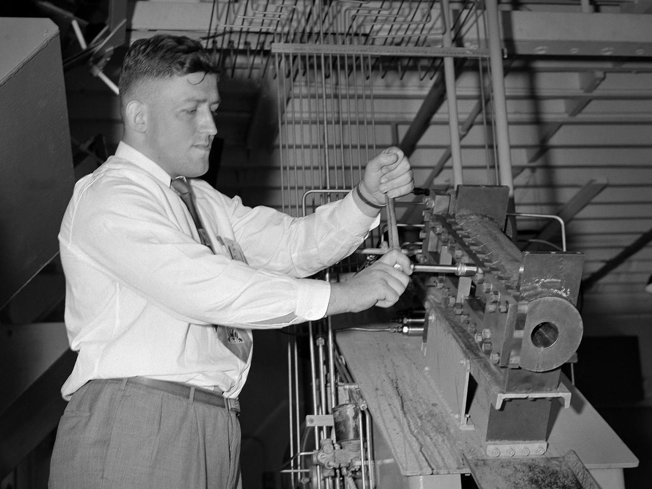 William Kerslake, a combustion researcher at the National Advisory Committee for Aeronautics (NACA) Lewis Flight Propulsion Laboratory, examines the setup of a transparent rocket in a Rocket Laboratory test cell. Kerslake joined NACA Lewis the previous summer after graduating from the Case Institute of Technology with a chemistry degree. His earliest professional research concentrated on combustion instability in small rocket engines.    While at Case the quiet, 250-pound Kerslake also demonstrated his athletic prowess on the wrestling team. He continued wrestling for roughly a decade afterwards while conducting his research with the NACA. Kerslake participated in Olympic competitions in Helsinki (1952), Melbourne (1956), and Rome (1960). He won 30 national championships in three different weight classes and captured the gold at the 1955 Pan American Games in Mexico City. Kerslake accomplished all this while maintaining his research career, raising a family, and paying his own expenses.     As his wrestling career was winding down in the early 1960s, Kerslake’s professional career changed, as well. He was transferred to Harold Kaufman’s Electrostatic Propulsion Systems Section in the new Electromagnetic Propulsion Division. Kaufman was developing the first successful ion engine at the time, and Kerslake spent the remainder of his career working in the electric propulsion field. He was heavily involved in the two Space Electric Rocket Test (SERT) missions which demonstrated that the ion thrusters could successfully operate in space. Kerslake retired in 1985 with over 30 years of service.
