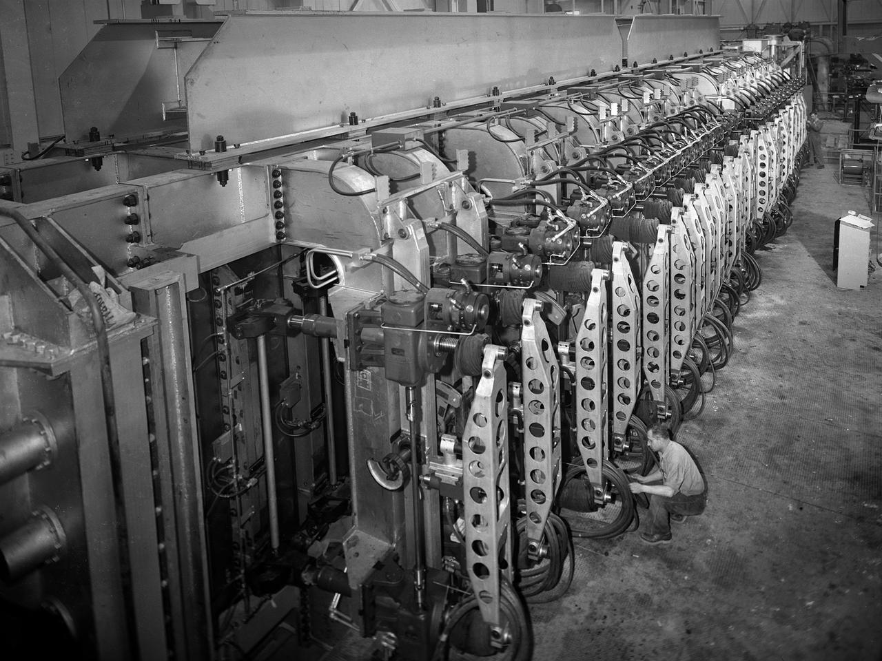A mechanic checks the tubing on one of the many jacks which control the nozzle section of the 10- by 10-Foot Supersonic Wind Tunnel at the National Advisory Committee for Aeronautics (NACA) Lewis Flight Propulsion Laboratory. The 10- by 10-foot tunnel, which had its official opening in May 1956, was built under the Congressional Unitary Plan Act which coordinated wind tunnel construction at the NACA, Air Force, industry, and universities. The 10- by 10 was the largest of the three NACA tunnels built under the act.      The 10- by 10 wind tunnel can be operated as a closed circuit for aerodynamic tests or as an open circuit for propulsion investigations. The 10-foot tall and 76-foot long stainless steel nozzle section just upstream from the test section can be adjusted to change the speed and composition of the air flow. Hydraulic jacks, seen in this photograph, flex the 1.37-inch thick walls of the tunnel nozzle. The size of the nozzle’s opening controls the velocity of the air through the test section.     Seven General Electric motors capable of generating 25,000 horsepower produce the Mach 2.5 and 2.5 airflows. The facility was mostly operated at night due to its large power load requirements.