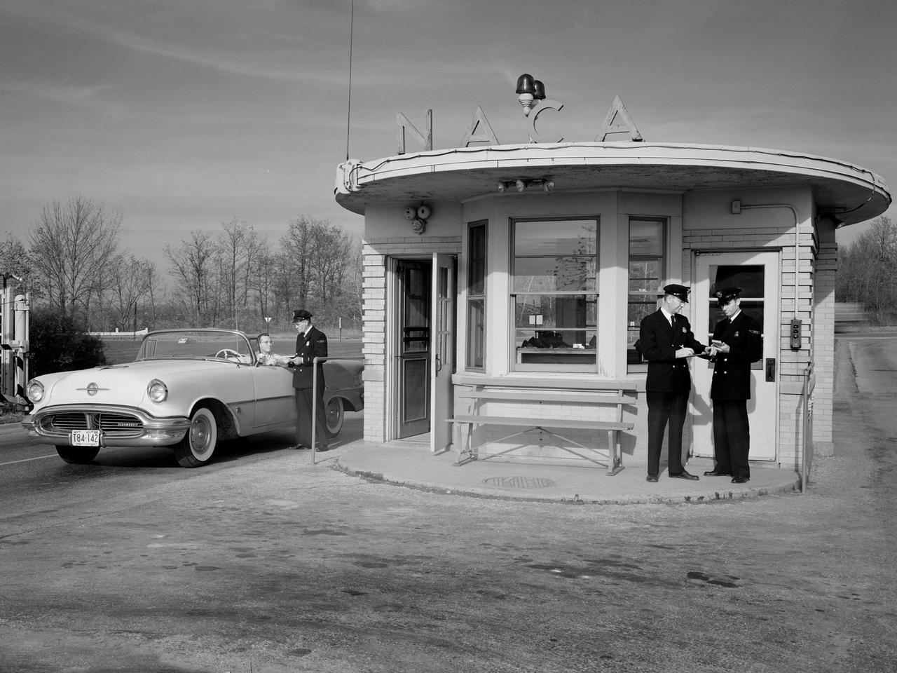 A vehicle leaves the National Advisory Committee for Aeronautics (NACA) Lewis Flight Propulsion Laboratory in Cleveland, Ohio. The guard house was on the main entrance to the laboratory from Brookpark Road. The original building was fairly small and easily crowded. In the early 1960s a new security facility was built several hundred feet beyond the original guard house. The original structure remained in place for several years, but was not utilized. The structure seen in this photograph was replaced in 2011 by a new building and entrance configuration.    In September 1955, approximately a year before this photo was taken, the security staff was given new navy blue uniforms, seen here.