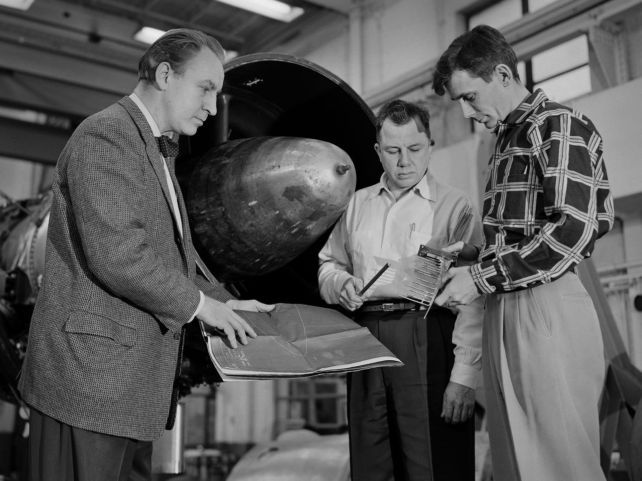 Researcher Bill Reiwaldt discusses the preparations for a test in the Altitude Wind Tunnel with technicians Jack Wagner and Dick Golladay at the National Advisory Committee for Aeronautics (NACA) Lewis Flight Propulsion Laboratory. Research engineers developed ideas for tests that were often in response to requests from the military or aircraft industry. Arrangements were made to obtain an engine for the study and to transport it to the Cleveland laboratory. The engine was brought into the facility’s shop area, where it was readied for investigation. It was common for several different engines to be worked on simultaneously in the shop.    The researcher would discuss the engine and the test objectives with the Test Installation Division and the facility’s technicians. The operations team would handle the installation of the instrumentation and fitting the test into the facility’s schedule. Upon completion of the previous test, the engine was removed. The next engine was lifted by an overhead crane and transported from the shop to the test section. The engine was connected to the measurement devices and fuel and oil supply lines. Engines were tested over numerous runs under varying conditions and with variations on the configuration. The findings and test procedure were then described in research or technical memorandums and distributed to industry.