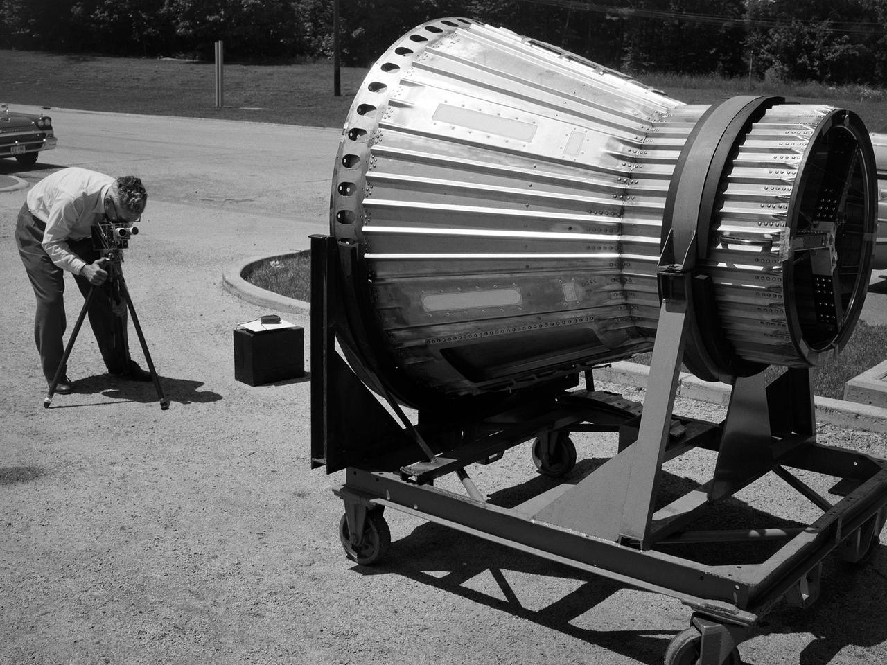 National Aeronautics and Space Administration (NASA) photographer Arthur Laufman sets up a camera to film a Mercury capsule that was constructed by the Lewis Research Center staff. Lewis engineers and mechanics built two of the capsules for the upcoming Big Joe launches in September 1959. Big Joe was an attempt early in Project Mercury to use a full-scale Atlas booster to simulate the reentry of a mock-up Mercury capsule without actually placing it in orbit.    The Photographic Branch, referred to as the Photo Lab, was part of the center’s Technical Reports Division. Originally the group performed normal and high-speed still image and motion picture photography. The photographers documented construction, performed publicity work, created images for reports, photographed data on manometer boards, and recorded test footage.   Laufman joined the Photo Lab staff in 1948 and began producing full-length technical films as a tool to educate those outside of the agency on the research being conducted at Lewis. He worked with engineers to determine proper subjects for these films and develop a script. Laufman not only filmed tests, but also supporting footage of facilities, models, and staff members. He then edited the footage and added audio, visuals, and narration. The film masters were assigned standard identification numbers and add to the Photo Lab’s catalogue.