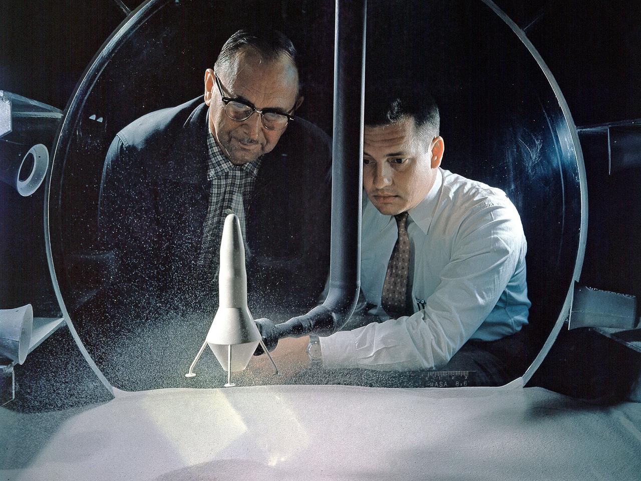 NASA Researchers view a demonstration of the moon dust simulator in the 8- by 6-Foot Supersonic Wind Tunnel facility at the National Aeronautics and Space Administration (NASA) Lewis Research Center. The researchers were studying the effect of the lunar lander’s retrorockets on the loose dust on the lunar surface. There was some concern that the retrorockets would kick up so much dust that the crew would lose the ability to see. They also did not know how the dust’s behavior would be affected by the space atmosphere. This small vacuum tank was built for very preliminary investigations into this matter. The pipe entering the top of the tank supplied the airflow to the lander model, which was affixed to the pipe. The researchers altered the vacuum levels and speed of the airflow.