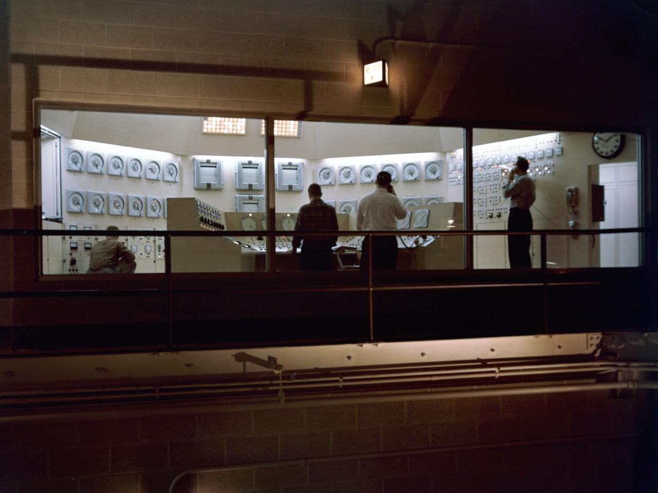 Operators test the National Aeronautics and Space Administration’s (NASA) Plum Brook Reactor Facility systems in the months leading up to its actual operation. The “Reactor On” signs are illuminated but the reactor core was not yet ready for chain reactions. Just a couple weeks after this photograph, Plum Brook Station held a media open house to unveil the 60-megawatt test reactor near Sandusky, Ohio. More than 60 members of the print media and radio and television news services met at the site to talk with community leaders and representatives from NASA and Atomic Energy Commission. The Plum Brook reactor went critical for the first time on the evening of June 14, 1961. It was not until April 1963 that the reactor reached its full potential of 60 megawatts.     The reactor control room, located on the second floor of the facility, was run by licensed operators. The operators manually operated the shim rods which adjusted the chain reaction in the reactor core. The regulating rods could partially or completely shut down the reactor.     The control room also housed remote area monitoring panels and other monitoring equipment that allowed operators to monitor radiation sensors located throughout the facility and to scram the reactor instantly if necessary. The color of the indicator lights corresponded with the elevation of the detectors in the various buildings. The reactor could also shut itself down automatically if the monitors detected any sudden irregularities.