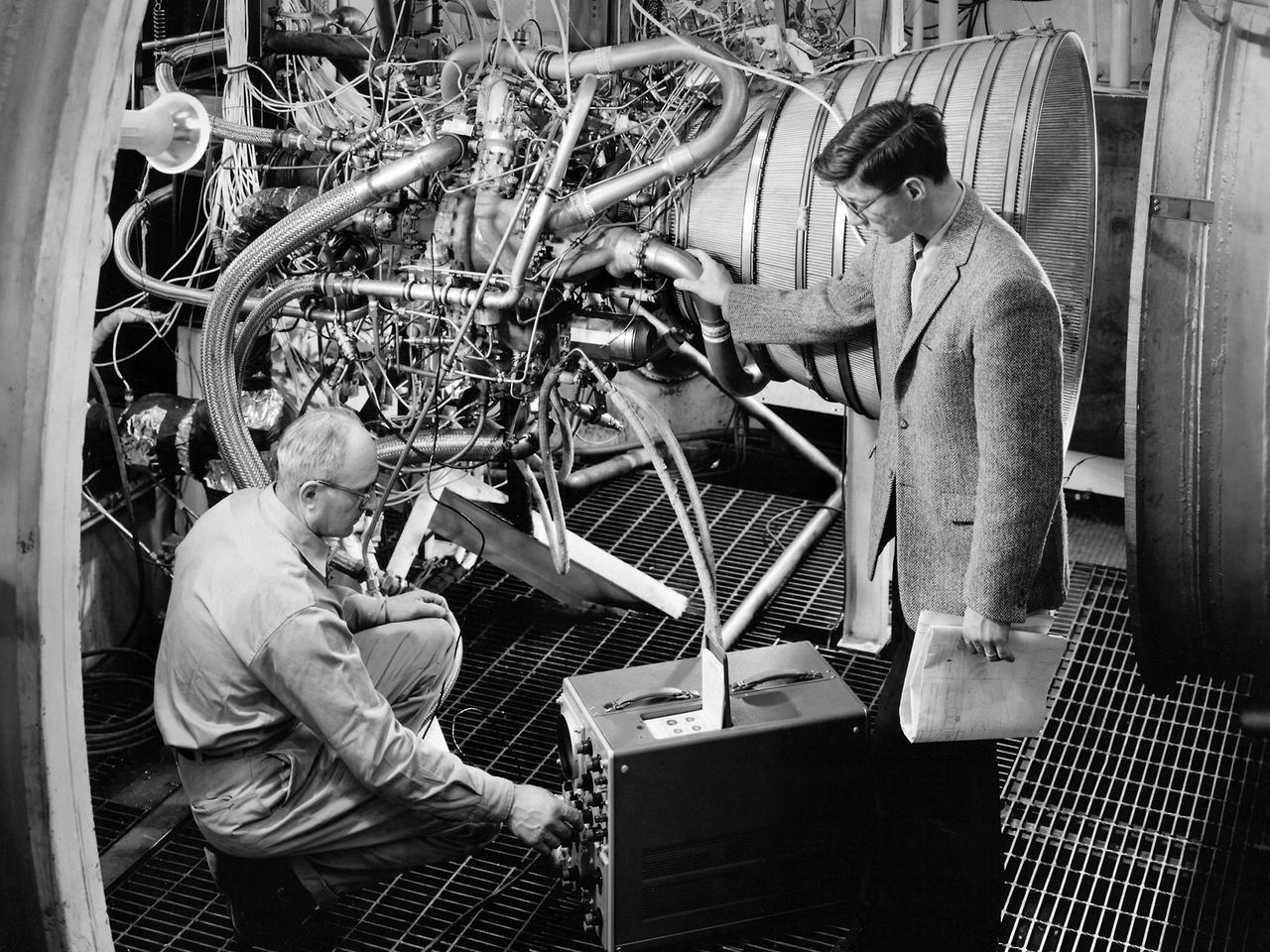 Lead Test Engineer John Kobak (right) and a technician use an oscilloscope to test the installation of a Pratt and Whitney RL-10 engine in the Propulsion Systems Laboratory at the National Aeronautics and Space Administration (NASA) Lewis Research Center. In 1955 the military asked Pratt and Whitney to develop hydrogen engines specifically for aircraft. The program was canceled in 1958, but Pratt and Whitney decided to use the experience to develop a liquid-hydrogen rocket engine, the RL-10. Two of the 15,000-pound-thrust RL-10 engines were used to power the new Centaur second-stage rocket. Centaur was designed to carry the Surveyor spacecraft on its mission to soft-land on the Moon. Pratt and Whitney ran into problems while testing the RL-10 at their facilities. NASA Headquarters assigned Lewis the responsibility for investigating the RL-10 problems because of the center’s long history of liquid-hydrogen development. Lewis’ Chemical Rocket Division began a series of tests to study the RL-10 at its Propulsion Systems Laboratory in March 1960. The facility contained two test chambers that could study powerful engines in simulated altitude conditions. The first series of RL-10 tests in early 1961 involved gimballing the engine as it fired. Lewis researchers were able to yaw and pitch the engine to simulate its behavior during a real flight.