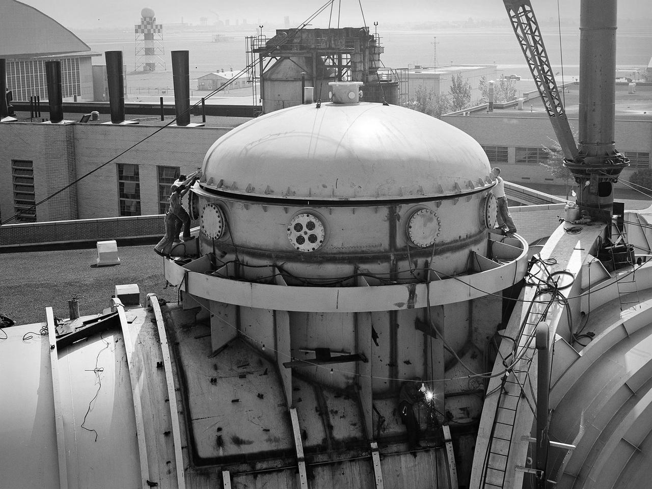 This 22.5-foot-diameter domed lid was added to the Space Power Chambers to allow the vertical installation of a Centaur second-stage rocket into the vacuum tank at the National Aeronautics and Space Administration (NASA) Lewis Research Center. The lid could be removed using a crane so that the Centaur could be lowered into the chamber. After a year of additional construction, the new dome and extension were completed in September 1963. The feature became the facility’s distinctive attribute. The modifications to the facility began two years earlier, however.    In 1961, NASA Lewis management decided to convert the Altitude Wind Tunnel into two large test chambers and later renamed it the Space Power Chambers. The conversion included the removal of the tunnel’s internal components and the insertion of bulkheads to seal off the new chambers within the tunnel. The 100-foot-long vacuum tank was created in the east leg of the tunnel, which was 31 feet in diameter at one end and 27 feet in diameter at the other.     With the transfer of the Centaur second-stage rocket program to NASA Lewis in October 1962, the newly completed Space Power Chambers facility had to be modified to accommodate the space vehicle. The goal of the test engineers was to subject the Centaur to long durations in conditions that would replicate those encountered during its missions in space. The facility was used for a variety of tests on the Centaur second-stage rocket until the early 1970s.