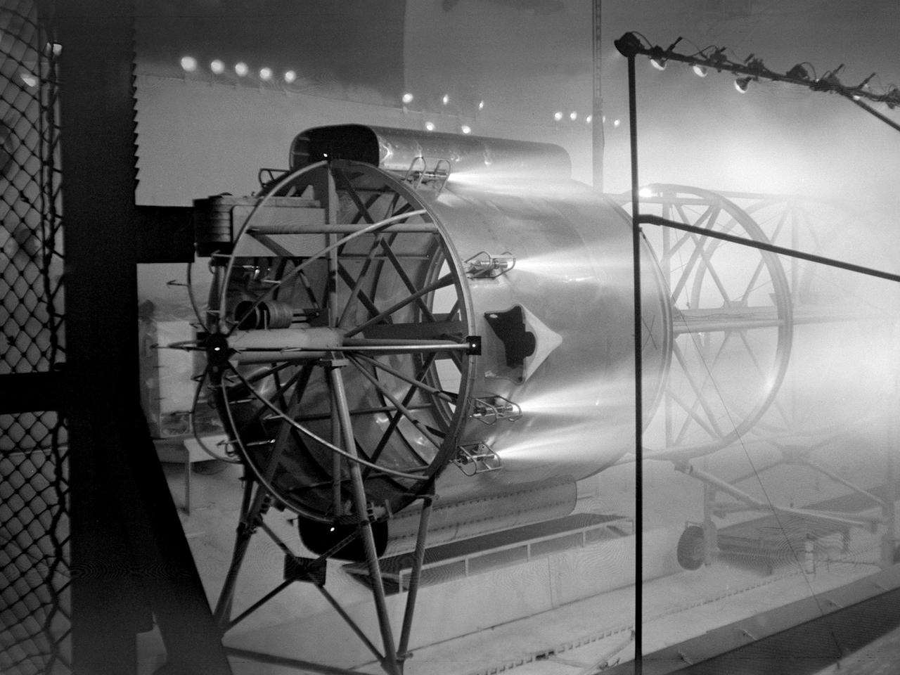 An Atlas/Centaur mass model undergoes a separation test inside the Space Power Chambers at NASA Lewis Research Center. Lewis was in the midst of an extensive effort to prepare the Centaur second-stage rocket for its missions to send the Surveyor spacecraft to the moon as a precursor to the Apollo missions. As part of these preparations, Lewis management decided to convert its Altitude Wind Tunnel into two large test chambers—the Space Power Chambers. The conversion included the removal of the tunnel’s internal components and the insertion of bulkheads to seal off the new chambers within the tunnel. One chamber could simulate conditions found at 100 miles altitude, while this larger chamber simulated the upper atmosphere.     In this test series, researchers wanted to verify that the vehicle’s retrorockets would properly separate the Centaur from the Atlas. The model was suspended horizontally on a trolley system inside chamber. A net was hung at one end to catch the jettisoned Atlas model. The chamber atmosphere was reduced to a pressure altitude of 100,000 feet, and high-speed cameras were synchronized to the ignition of the retrorockets.   The simulated Centaur is seen here jettisoning from the Atlas out of view to the right. The study resulted in a new jettison method that would significantly reduce the separation time and thus minimize the danger of collision between the two stages during separation.