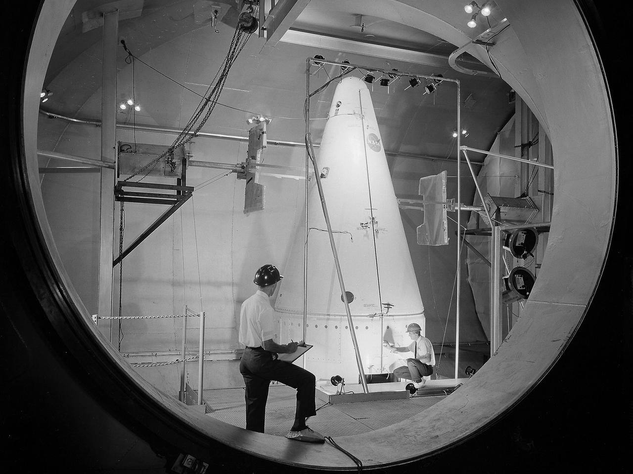 Researchers prepare a Centaur-Surveyor nose cone shroud for a separation test in the Space Power Chambers at the National Aeronautics and Space Administration (NASA) Lewis Research Center. Lewis was in the midst of an extensive effort to prepare the Centaur second-stage rocket for its missions to send the Surveyor spacecraft to the moon as a precursor to the Apollo missions. The nose fairing provided an aerodynamic shield for the payload, guidance system, and electronics package as the rocket traveled through the Earth’s atmosphere. Upon entering space, the thruster near the tip of the fairing forced the two pieces away from the space vehicle. The June 30, 1964 launch of Atlas-Centaur-3 was successful.    Within a month of the launch, a Centaur shroud was obtained and installed in the Space Power Chambers. The facility was the only space tank in the country large enough to accommodate the hardware. The two halves of the fiberglass fairing were mounted vertically to a platform. Aluminum pads were set up on either side to catch the shroud halves as they were jettisoned, and a myriad of high-speed cameras were installed to record the tests.    The shroud was badly damaged during the first test. It was replaced, and the test equipment redesigned. Over the course of 11 runs during the summer of 1964, the redesigned bulkhead was retested and the new fairing was validated by the final jettison on November 24, 1964. Just over two weeks later, Atlas-Centaur-4 successfully launched a mock-up Surveyor spacecraft into orbit. It was the first Centaur mission to have an error-free shroud jettison.