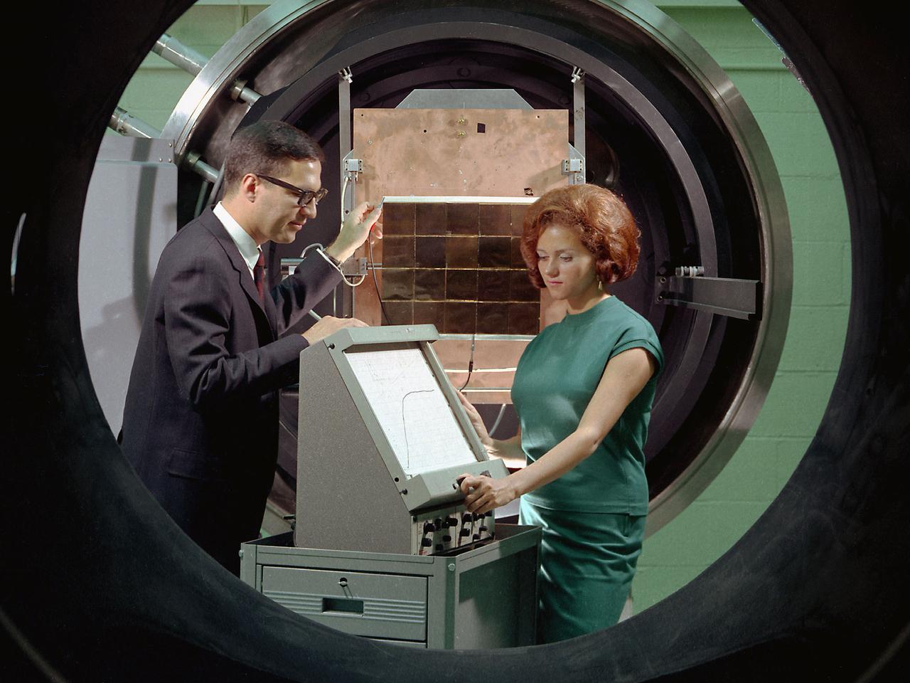 George Mazaris, works with an assistant to obtain the preliminary measurements of cadmium sulfide thin-film solar cells being tested in the Space Environmental Chamber at the National Aeronautics and Space Administration (NASA) Lewis Research Center. Lewis’ Photovoltaic Fundamentals Section was investigating thin-film alternatives to the standard rigid and fragile solar cells. The cadmium sulfide semiconductors were placed in a light, metallized substrate that could be rolled or furled during launch. The main advantage of the thin-film solar cells was their reduced weight. Lewis researchers, however, were still working on improving the performance of the semiconductor.    The new thin-film solar cells were tested in a space simulation chamber in the CW-6 test cell in the Engine Research Building. The chamber created a simulated altitude of 200 miles. Sunlight was simulated by a 5000-watt xenon light. Some two dozen cells were exposed to 15 minutes of light followed by 15 minutes of darkness to test their durability in the constantly changing illumination of Earth orbit.   This photograph was taken for use in a NASA recruiting publication.