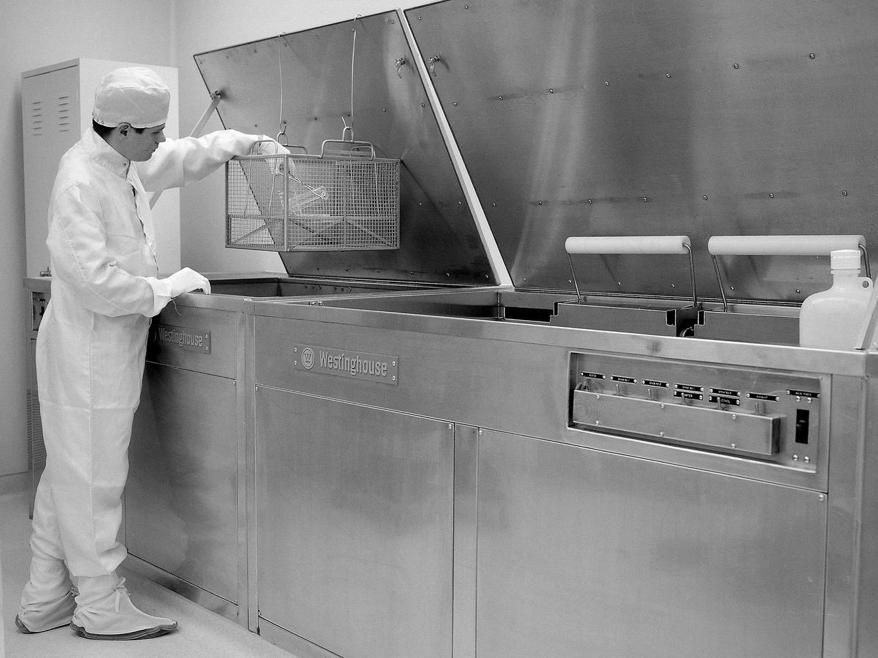 A technician prepares a test sample in the Zero Gravity Research Facility clean room at the National Aeronautics and Space Administration (NASA) Lewis Research Center. The Zero Gravity Research Facility contained a drop tower which provided five seconds of microgravity during freefall in its 450-foot deep vacuum chamber. The facility has been used for a variety of studies relating to the behavior of fluids and flames in microgravity.    During normal operations, a cylindrical 3-foot diameter and 11-foot long vehicle was used to house the experiments, instrumentation, and high speed cameras. The 4.5-foot long and 1.5-foot wide rectangular vehicle, seen in this photograph, was used less frequently. A 3-foot diameter orb was used for the special ten-second drops in which the package was pneumatically shot to the top of the tower then dropped. The facility also contained a control room, shop offices, tool and equipment rooms, and this clean room.    The 242.5-foot long and 19.5-foot wide clean room was equipped with specialized cleaning equipment. In the 1960s the room was rated as a class 10,000 clean room, but I was capable of meeting the class 100 requirements. The room included a fume hood, ultrasonic cleaner, and a laminar flow station which operated as a class 100 environment. The environment in the clean room was maintained at 71° F and a relative humidity of 45- percent.