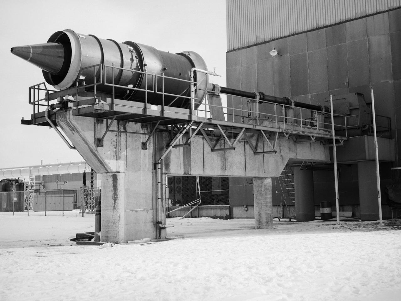 The Fan Noise Test Facility built at the Lewis Research Center to obtain far-field noise data for the National Aeronautics and Space Administration (NASA) and General Electric Quiet Engine Program. The engine incorporated existing noise reduction methods into an engine of similar power to those that propelled the Boeing 707 or McDonnell-Douglas DC-8 airliner. The new the low-bypass ratio turbofan engines of the 1960s were inherently quieter than their turbojet counterparts, researchers had a better grasp of the noise generation problem, and new acoustic technologies had emerged.     Lewis contracted General Electric in 1969 to build and aerodynamically test three experimental engines with 72-inch diameter fans. The engines were then brought to Lewis and tested with an acoustically treated nacelle. This Fan Noise Test Facility was built off of the 10- by 10-Foot Supersonic Wind Tunnel’s Main Compressor and Drive Building. Lewis researchers were able to isolate the fan’s noise during these initial tests by removing the core of the engine. The Lewis test rig drove engines to takeoff tip speeds of 1160 feet per second. The facility was later used to test a series of full-scale model fans and fan noise suppressors to be used with the quiet engine.      NASA researchers predicted low-speed single-stage fans without inlet guide vanes and with large spacing between rotors and stators would be quieter. General Electric modified a TF39 turbofan engine by removing the the outer protion of the fan and spacing the blade rows of the inner portion. The tests revealed that the untreated version of the engine generated less noise than was anticipated, and the acoustically treated nacelle substantially reduced engine noise.