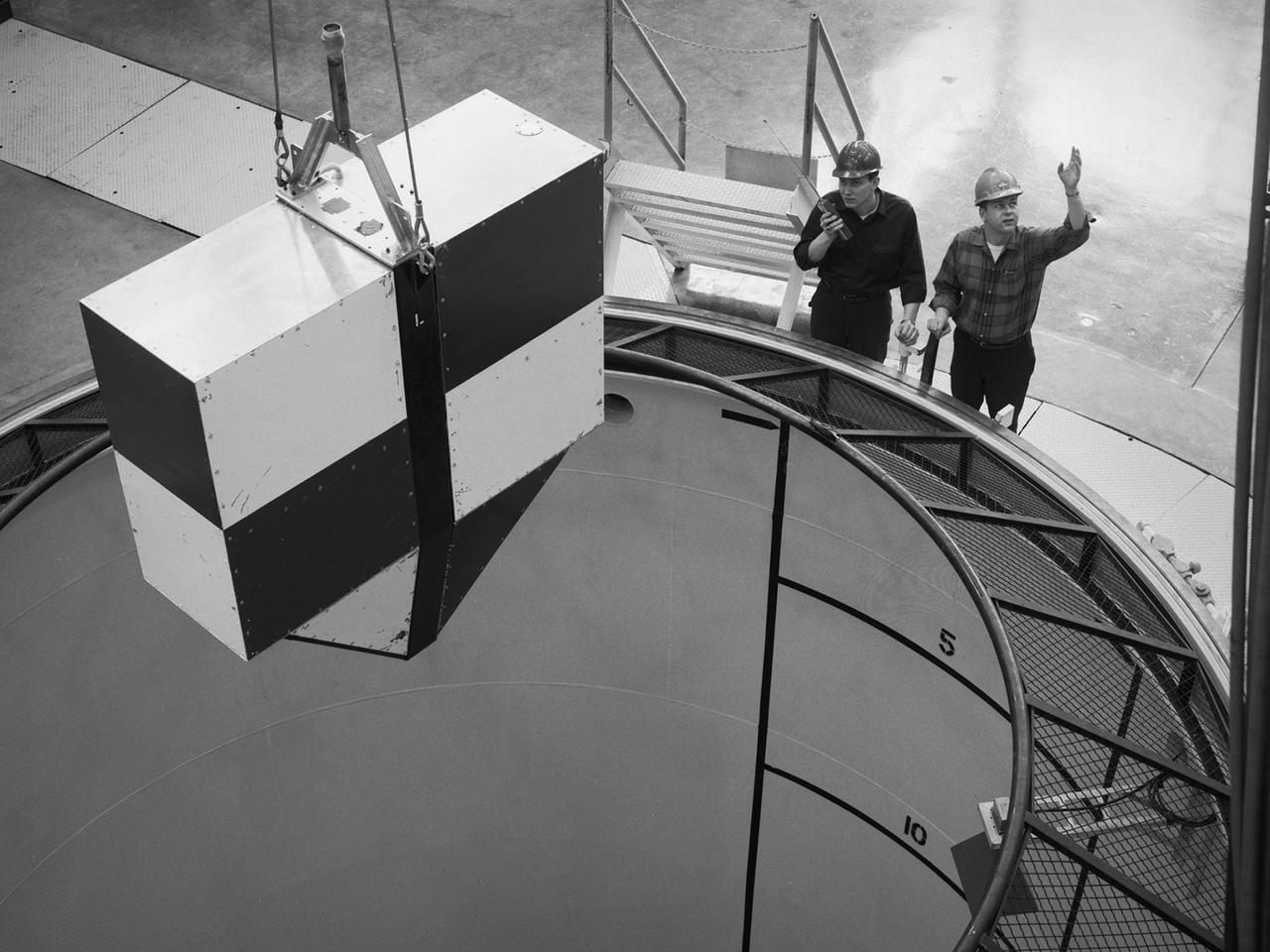 A rectangular drop test vehicle perched above 450-foot shaft at the Zero Gravity Research Facility at NASA Lewis Research Center. The drop tower was designed to provide five seconds of microgravity during a normal drop, but had a pneumatic gun that could quickly propel the vehicle to the top of the shaft prior to its drop, thus providing ten seconds of microgravity. The shaft contained a steel-lined vacuum chamber 20 feet in diameter and 469 feet deep. The package was stopped at the bottom of the pit by a 15-foot deep deceleration cart filled with polystyrene pellets.    During normal operations, a cylindrical 3-foot diameter and 11-foot long vehicle was used to house the experiments, instrumentation, and high speed cameras. The 4.5-foot long and 1.5-foot wide rectangular vehicle, seen in this photograph, was used less frequently. A 3-foot diameter orb was used for the ten second drops.    After the test vehicle was prepared it was suspended above the shaft from the top of the chamber. A lid was used to seal the top of the chamber. The vacuum system reduced the pressure levels inside the chamber. The bolt holding the vehicle was then sheared and the vehicle plummeted into the deceleration cart.