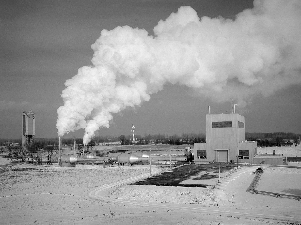 The Space Propulsion Research Facility, better known as B-2, operating at the National Aeronautics and Space Administration’s (NASA) Plum Brook Station in Sandusky, Ohio. B-2 is the world's only high altitude test facility capable of full-scale rocket engine and launch vehicle system level tests. It was created to test rocket propulsion systems with up to 100,000 pounds of thrust in a simulated space environment. The facility has the unique ability to maintain a vacuum at the rocket’s nozzle while the engine is firing. The rocket fires into a 120-foot deep spray chamber which cools the exhaust before it is ejected outside the facility. B-2 simulated space using giant diffusion pumps to reduce chamber pressure, nitrogen-filled cold walls create cryogenic temperatures, and quartz lamps replicate the radiation of the sun.       This photograph shows the facility undergoing check-out runs prior to its first test in late 1969.The 38-foot diameter and 62-foot tall vacuum chamber is inside the high-bay on the right. Below that is a 67-foot diameter and 120-foot deep spray chamber. The hot rocket exhaust is cooled in the chamber by a spray of 250,000 gallons of water per minute.    B-2’s first test was a hot firing of Centaur D-1A rocket on December 18, 1969. Since then the facility has fired more than 100 Pratt and Whitney RL-10 engines during the Centaur development, 80 current RL-10B-2 engines for Delta-3 development, and another 12 RL-10B-2s for the Delta 3 Upper Stage.