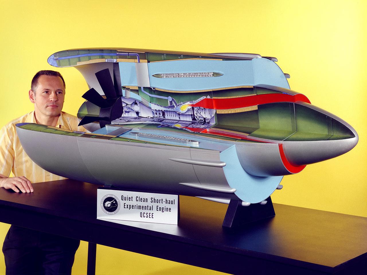 Program manager Carl Ciepluch poses with a model of the Quiet Clean Short Haul Experimental Engine (QCSEE) conceived by the National Aeronautics and Space Administration (NASA) Lewis Research Center. The QCSEE engine was designed to power future short-distance transport aircraft without generating significant levels of noise or pollution and without hindering performance. The engines were designed to be utilized on aircraft operating from small airports with short runways. Lewis researchers investigated two powered-lift designs and an array of new technologies to deal with the shorter runways.     Lewis contracted General Electric to design the two QCSEE engines—one with over-the-wing power-lift and one with an under-the-wing design. A scale model of the over-the-wing engine was tested in the Full Scale Tunnel at the Langley Research Center in 1975 and 1976. Lewis researchers investigated both versions in a specially-designed test stand, the Engine Noise Test Facility, on the hangar apron.     The QCSEE engines met the goals set out by the NASA researchers. The aircraft industry, however, never built the short-distance transport aircraft for which the engines were intended. Different technological elements of the engine, however, were applied to some future General Electric engines.
