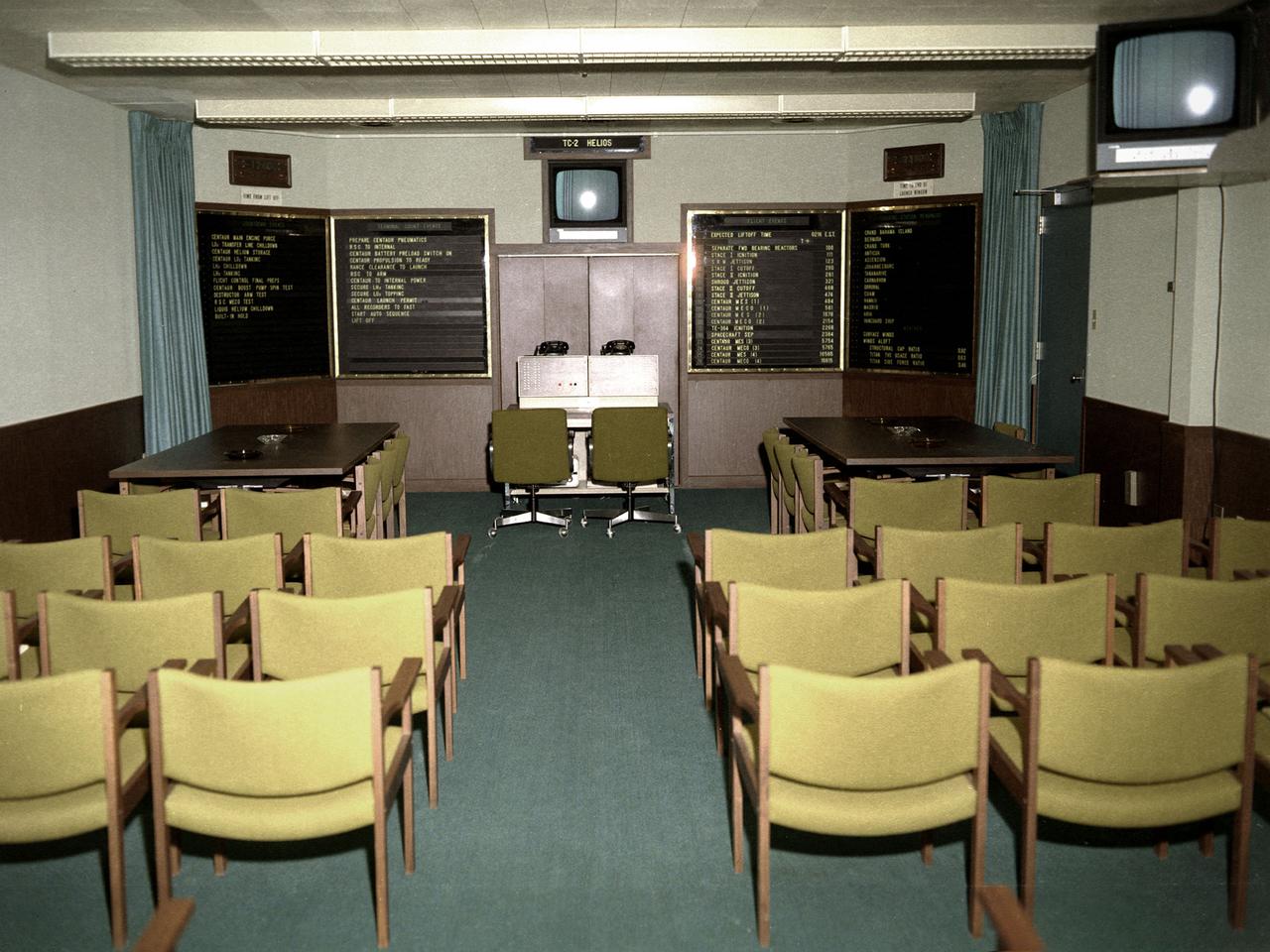 A Centaur rocket control room in the Development Engineering Building (DEB) at the National Aeronautics and Space Administration (NASA) Lewis Research Center in Cleveland, Ohio. The DEB, completed in the mid-1960s, provided office space for several hundred development engineers outside the center’s main gate. The location of the DEB emphasized the development staff’s separation from the research side of the laboratory.     This control room at Lewis was directly linked to Cape Kennedy. The Lewis staff in Cleveland could monitor and back up the Lewis launch team in the actual control room at the Cape. This photograph was taken during the preparations for the Titan-Centaur-Helios launch on December 10, 1974. The panels to the left listed the countdown events for the Centaur rocket. The launch countdown clock can be seen above these panels. The two panels on the right listed events predicted to occur during the flight and the availability of the tracking stations. The clock above the panels indicated the time remaining before the launch window expired.   The Launch Vehicles Division was created in 1969 to manage the launches of all Centaur and Agena rockets. The Launch Vehicles Division worked with the engineers to design the payload in a manner that ensured that its size and weight were within Centaur’s parameters. They also developed the proper trajectory analysis for the launch. These trajectories often had to be adjusted if the launch did not occur on the planned date.