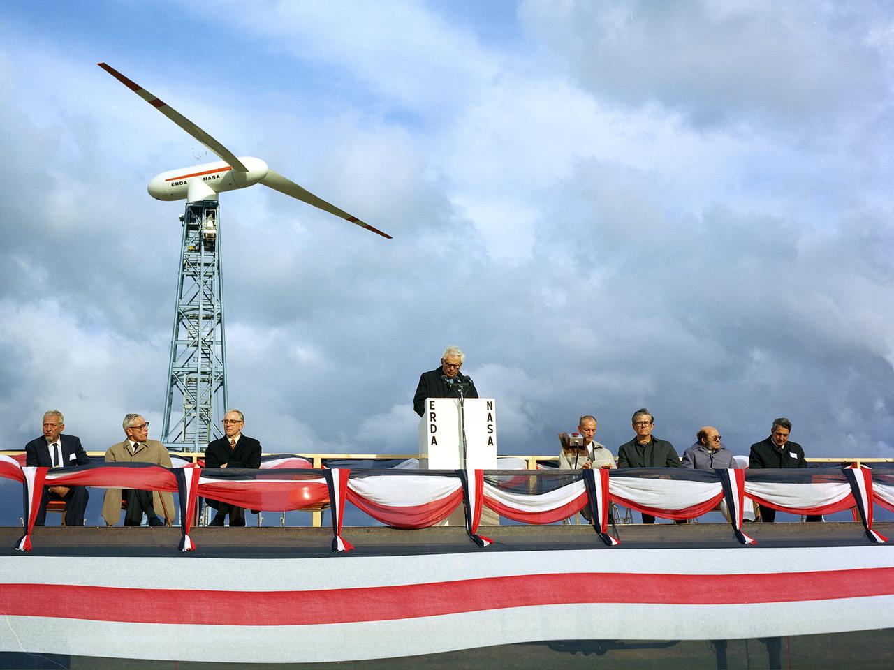Energy Research and Development Administration (ERDA) Administrator Robert Seamans addresses the crowd at the dedication ceremony for the Mod-0 100-kilowatt wind turbine at the National Aeronautics and Space Administration’s (NASA) Plum Brook Station. The wind turbine program was a joint NASA/ERDA effort to develop less expensive forms of energy during the 1970s. NASA Lewis was able to use its experience with aerodynamics, powerplants, and energy transfer to develop efficient and cost-effective wind energy systems. The Plum Brook wind turbine was the first of a series of increasingly powerful NASA-ERDA wind turbines built around the nation. From left to right: Congressional Committee aide John Dugan, retired S. Morgan Smith Company chief engineer Carl Wilcox, windmill pioneer Beauchamp Smith, NASA Administrator James Fletcher, Seamans, and Lewis Center Director Bruce Lundin. The three men to the right are unidentified.