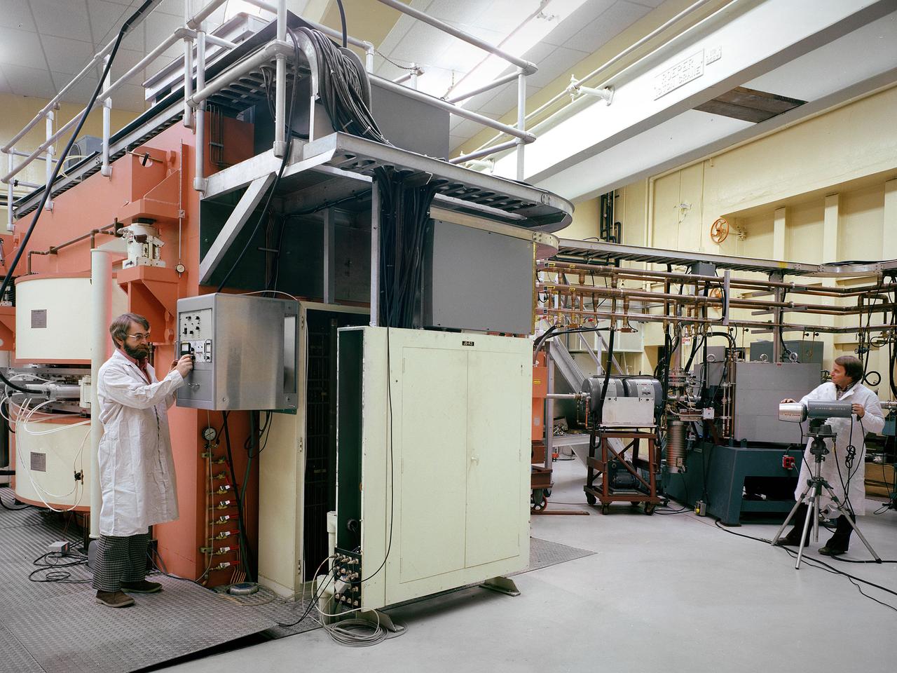 Researchers check the cyclotron in the Materials and Stresses Building at the National Aeronautics and Space Administration (NASA) Lewis Research Center. The Materials and Stresses Building, built in 1949, contained a number of laboratories to test the strength, diffusion, and other facets of materials. The materials could be subjected to high temperatures, high stresses, corrosion, irradiation, and hot gasses. The Physics of Solids Laboratory included a cyclotron, cloud chamber, helium cryostat, and metallurgy cave.     The cyclotron was built in the early 1950s to test the effects of radiation on different materials so that the proper materials could be used to construct a nuclear aircraft engine and other components. By the late 1950s, the focus had shifted to similar studies for rockets. NASA cancelled its entire nuclear program in January 1973, and the cyclotron was mothballed.    In 1975 the Cleveland Clinic Foundation partnered with NASA Lewis to use the cyclotron to treat cancer patients with a new type of radiation therapy. The cyclotron split beryllium atoms which caused neutrons to be released. The neutrons were streamed directly at the patient’s tumor. Over the course of five years, the cyclotron was used to treat 1200 patients. The program was terminated in 1980 as the Clinic shifted its efforts to concentrate on non-radiation treatments. The Lewis cyclotron was mothballed for a number of years before being demolished.