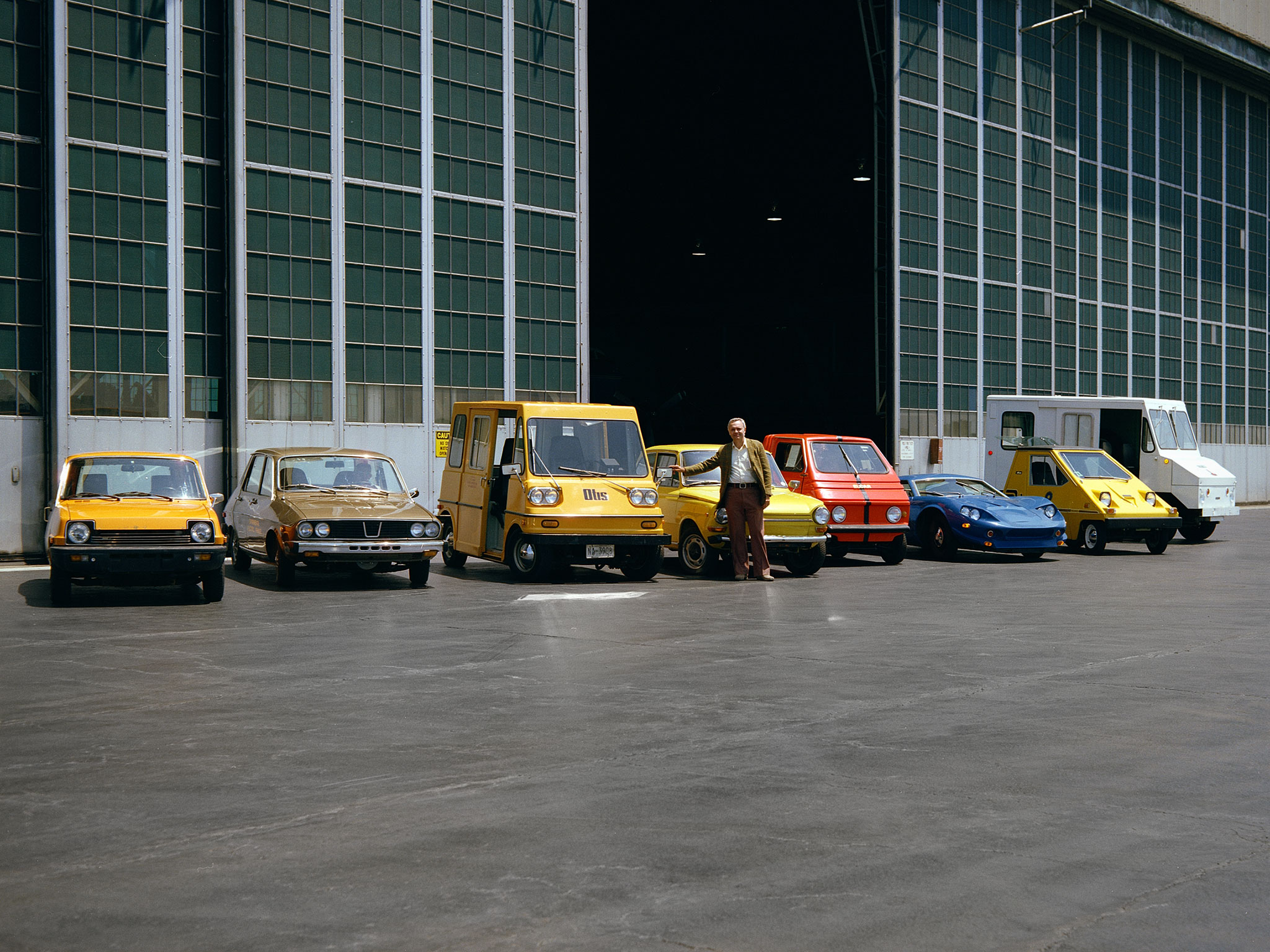 A series of brightly-colored electric vehicles are parked in a row outside the hangar at Glenn