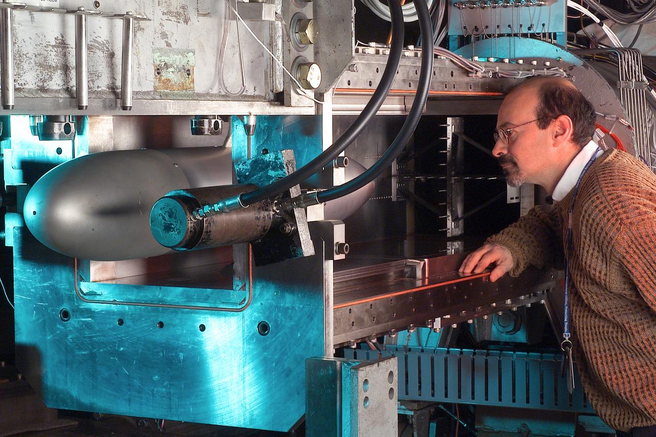 A researcher stands next to the Pulsed Ejector Wave Propagation Test Rig in an opened section of the 1'x1' Supersonic Wind Tunnel at NASA Glenn Research Center.