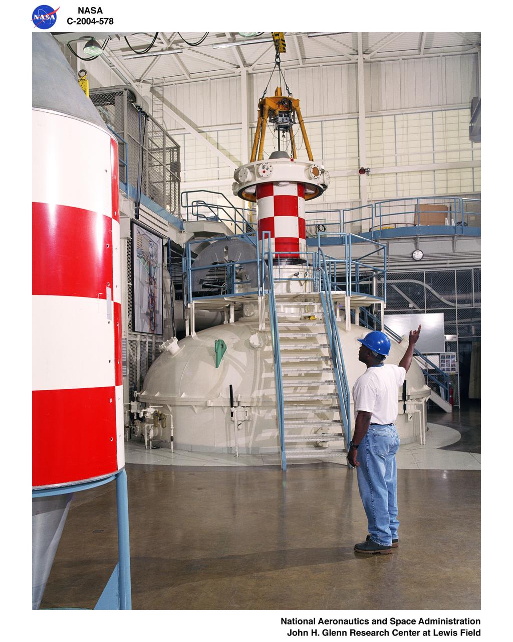 Floor view of drop vehicle and release mechanism being positioned over the vacuum chamber with a technician signaling the crane operator – Zero Gravity Research Facility.
