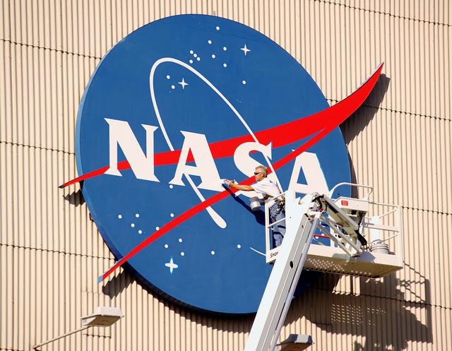 NASA image: Painter applies fresh coat of paint to the NASA Meatball on the Hangar's North Facade
