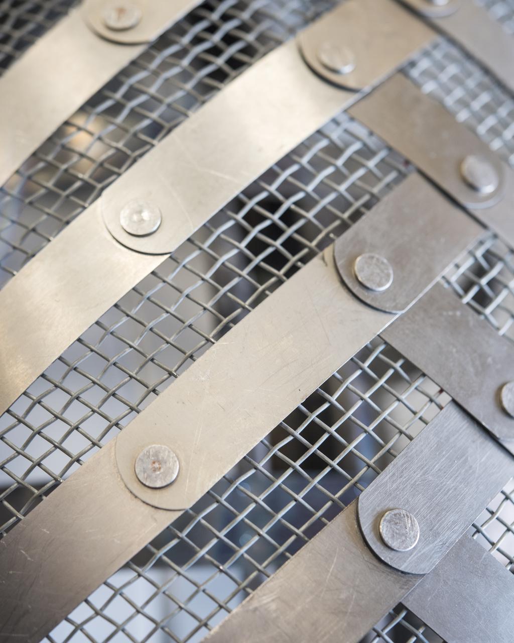 This is a close-up of an exact replica of the Apollo-era Lunar Roving Vehicle Wheel, of which twelve originals still rest on the surface of the Moon. The tire was designed to flex under load, without air, and was formed from a mesh of plated piano wire. Metal straps were hand riveted onto the mesh to reduce sinking into loose lunar soils.  These replica wheels were tested in NASA Glenn's SLOPE Lab to establish a baseline for future improvements.