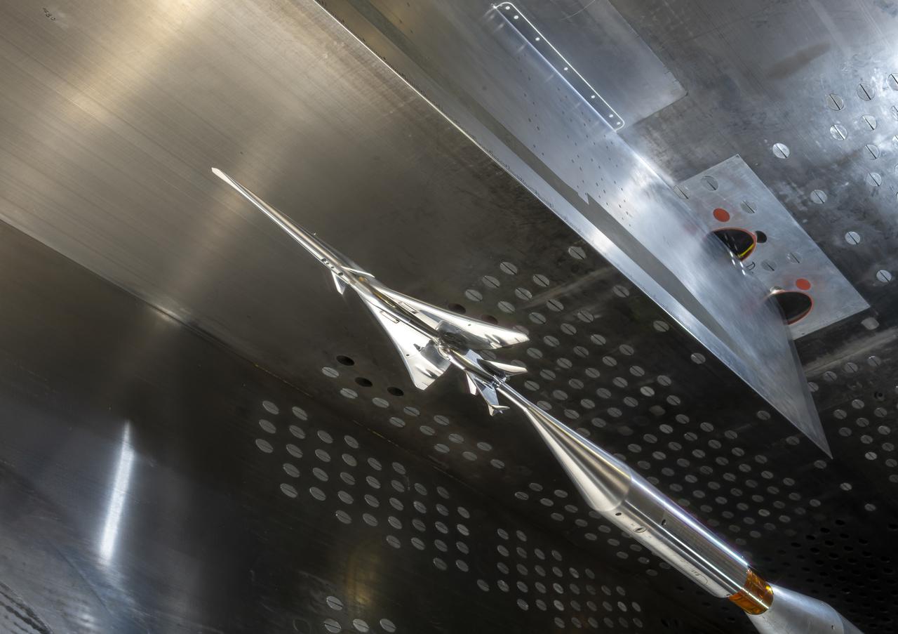 The X-59 Commercial Supersonic Transport model is installed upside down in the test section of the GRC 8x6 Supersonic wind tunnel.  The blade hanging from the top of the tunnel will be measuring the shock waves coming from the bottom of the model during testing.  The shock waves coming from the bottom of the model represent the sonic boom reaching the ground during flight.  The shape of the model is designed so as to greatly reduce the shock waves to prevent the typical boom coming from a supersonic aircraft.  Commercial Supersonic Transport, CST Project, X-59 Sonic Boom Test Model, in the 8x6-foot Supersonic Wind Tunnel, SWT