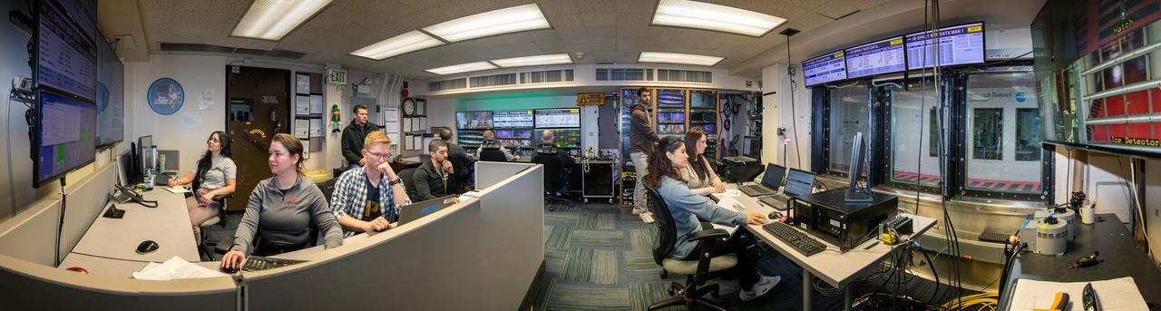Panorama of the IRT engineering and ice cloud calibration team in the control room.  Shown on the left are the data and system engineers.  In the center with their backs to the camera are the wind tunnel operators who control the wind speed and super cooled water flow.  In the center right of the photo is the video recording system and the test engineers.  On the right side the test section can be see though the wind and the TV screen shows the pray bars that create the icing cloud.