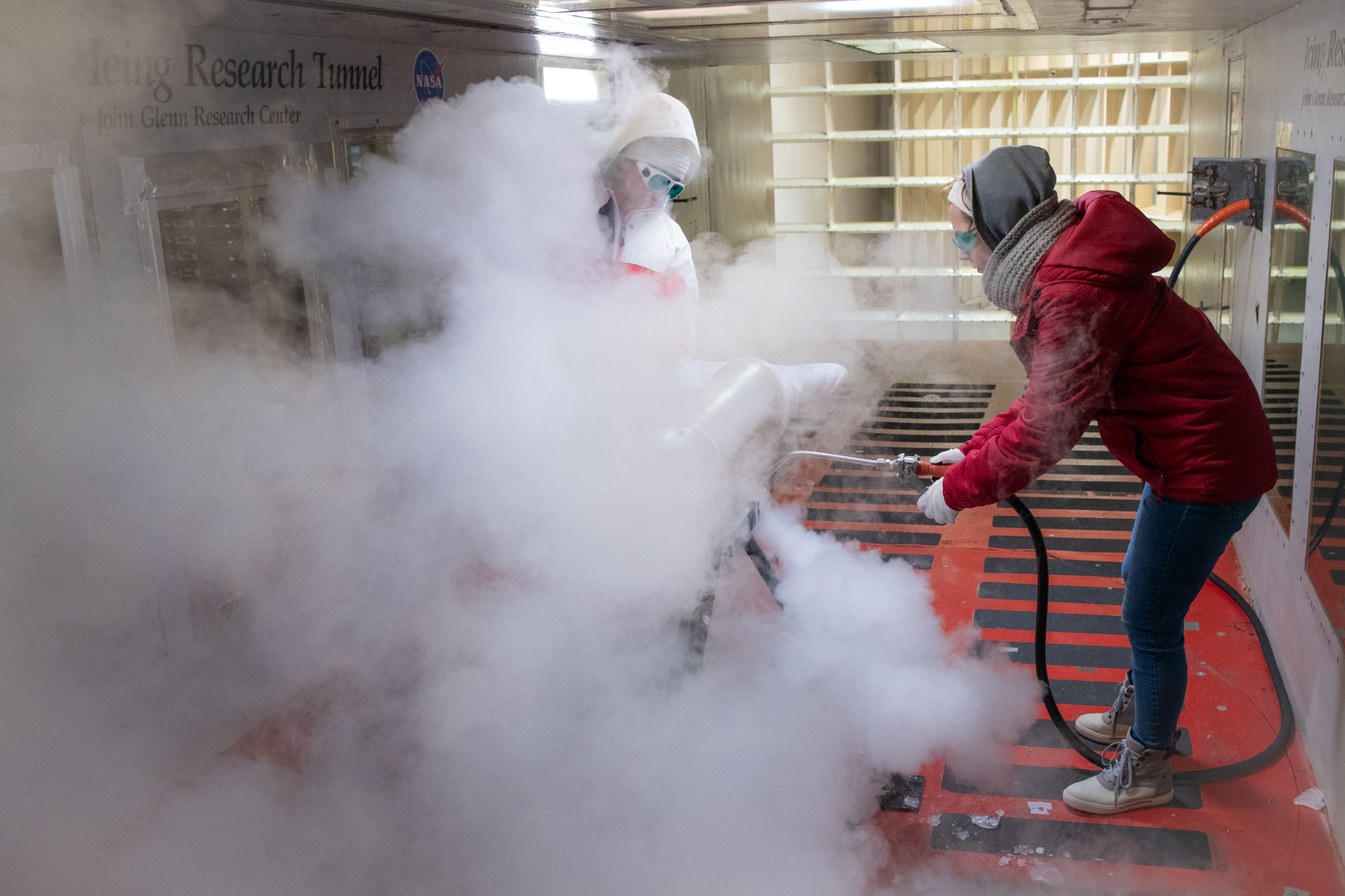 Test engineers clean the ice cloud detection probe in the Icing Research Tunnel in between test runs.  Steam is used to melt the accumulated ice on the detection probe.  The test engineers need to wear goggles to protect them from the laser light that the probe emits.  The laser detects water content and ice particles in the cloud that the wind tunnel produces.  This process is done to calibrate the tunnel for research by characterizing the cloud flow.
