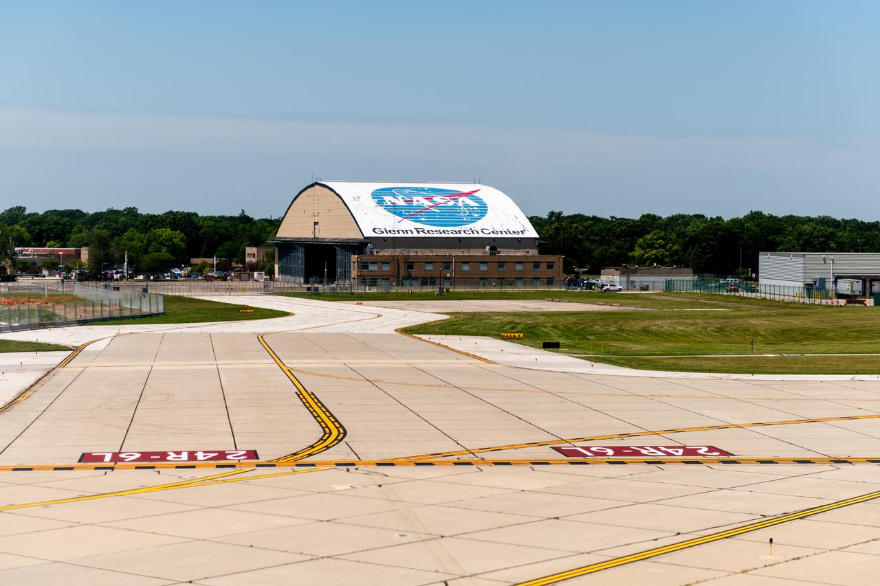 View of the Glenn Research Center Hangar from the Cleveland Hopkins Airport Runway during a testing flight on June 13, 2024.   A team at NASA’s Glenn Research Center in Cleveland streamed 4K video footage from an aircraft to the International Space Station and back for the first time using optical, or laser, communications. The feat was part of a series of tests on new technology that could provide live video coverage of astronauts on the Moon during the Artemis missions.  Working with the Air Force Research Laboratory and NASA’s Small Business Innovation Research program, Glenn engineers temporarily installed a portable laser terminal on the belly of a Pilatus PC-12 aircraft. They then flew over Lake Erie sending data from the aircraft to an optical ground station in Cleveland. From there, it was sent over an Earth-based network to NASA’s White Sands Test Facility in Las Cruces, New Mexico, where scientists used infrared light signals to send the data. Photo Credit: (NASA/Sara Lowthian-Hanna)
