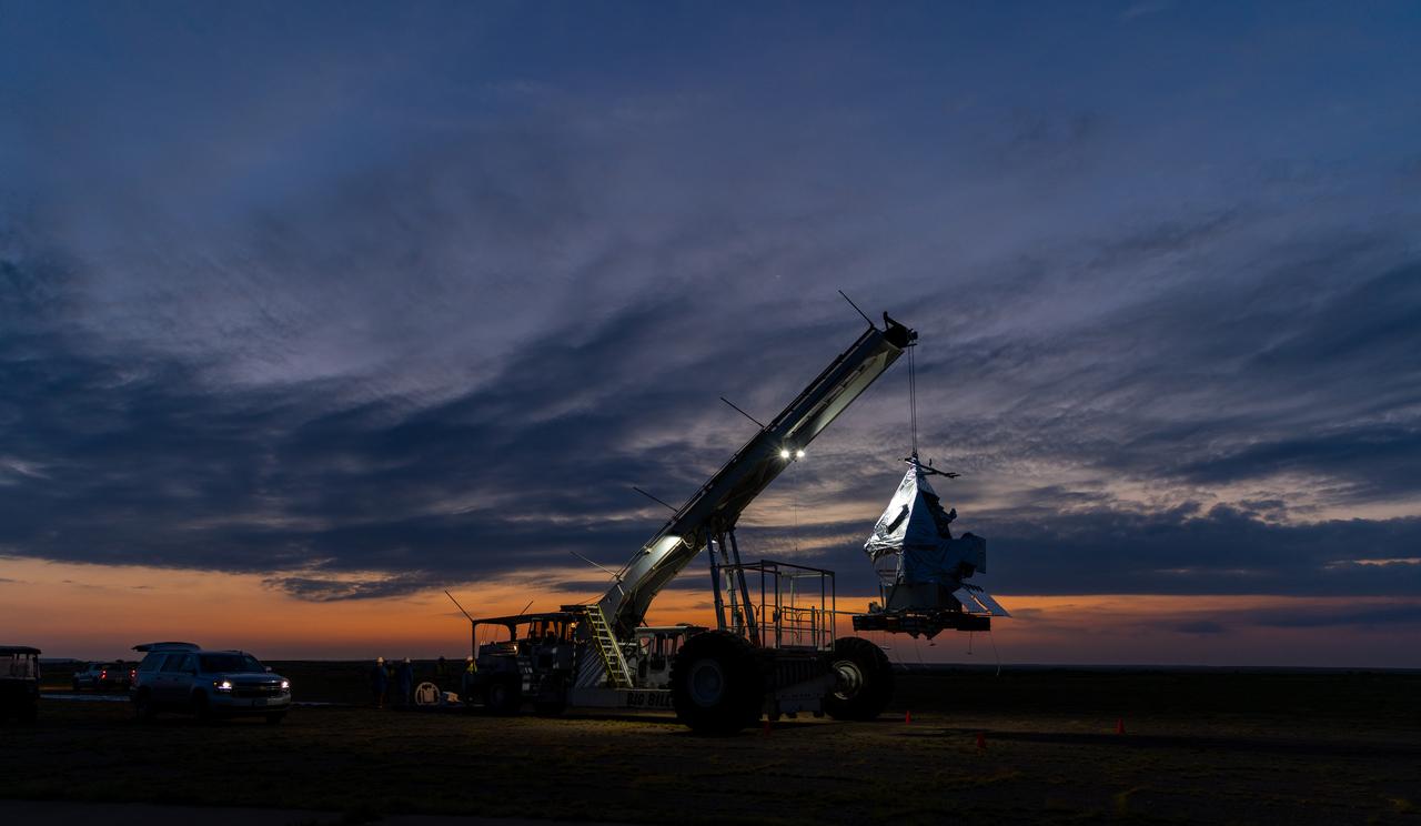 NASA Goddard astrophysicist Kyle Helson looks at EXCITE (EXoplanet Climate Infrared TElescope) as it dangles from the ceiling of a hangar at NASA’s Columbia Scientific Balloon Facility in Fort Sumner, New Mexico.