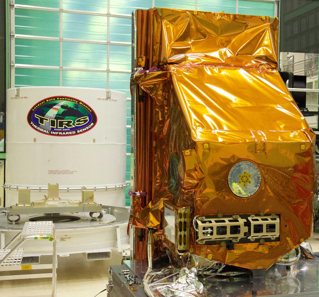 The TIRS instrument in the foreground with its shipping container waits in the background. The copper-color of TIRS is due to the gold-colored foil that coats the Multi-Layer Insulation blankets.  The Thermal Infrared Sensor (TIRS) will fly on the next Landsat satellite, the Landsat Data Continuity Mission (LDCM).  TIRS was built on an accelerated schedule at NASA's Goddard Space Flight Center, Greenbelt, Md. and will now be integrated into the LDCM spacecraft at Orbital Science Corp. in Gilbert, Ariz.   The Landsat Program is a series of Earth observing satellite missions jointly managed by NASA and the U.S. Geological Survey. Landsat satellites have been consistently gathering data about our planet since 1972. They continue to improve and expand this unparalleled record of Earth's changing landscapes for the benefit of all.  For more information on Landsat, visit:  <a href="http://www.nasa.gov/landsat" rel="nofollow">www.nasa.gov/landsat</a>  Credit: NASA/GSFC/Rebecca Roth  <b><a href="http://www.nasa.gov/audience/formedia/features/MP_Photo_Guidelines.html" rel="nofollow">NASA image use policy.</a></b>  <b><a href="http://www.nasa.gov/centers/goddard/home/index.html" rel="nofollow">NASA Goddard Space Flight Center</a></b> enables NASA’s mission through four scientific endeavors: Earth Science, Heliophysics, Solar System Exploration, and Astrophysics. Goddard plays a leading role in NASA’s accomplishments by contributing compelling scientific knowledge to advance the Agency’s mission.  <b>Follow us on <a href="http://twitter.com/NASA_GoddardPix" rel="nofollow">Twitter</a></b>  <b>Like us on <a href="http://www.facebook.com/pages/Greenbelt-MD/NASA-Goddard/395013845897?ref=tsd" rel="nofollow">Facebook</a></b>  <b>Find us on <a href="http://instagrid.me/nasagoddard/?vm=grid" rel="nofollow">Instagram</a></b>