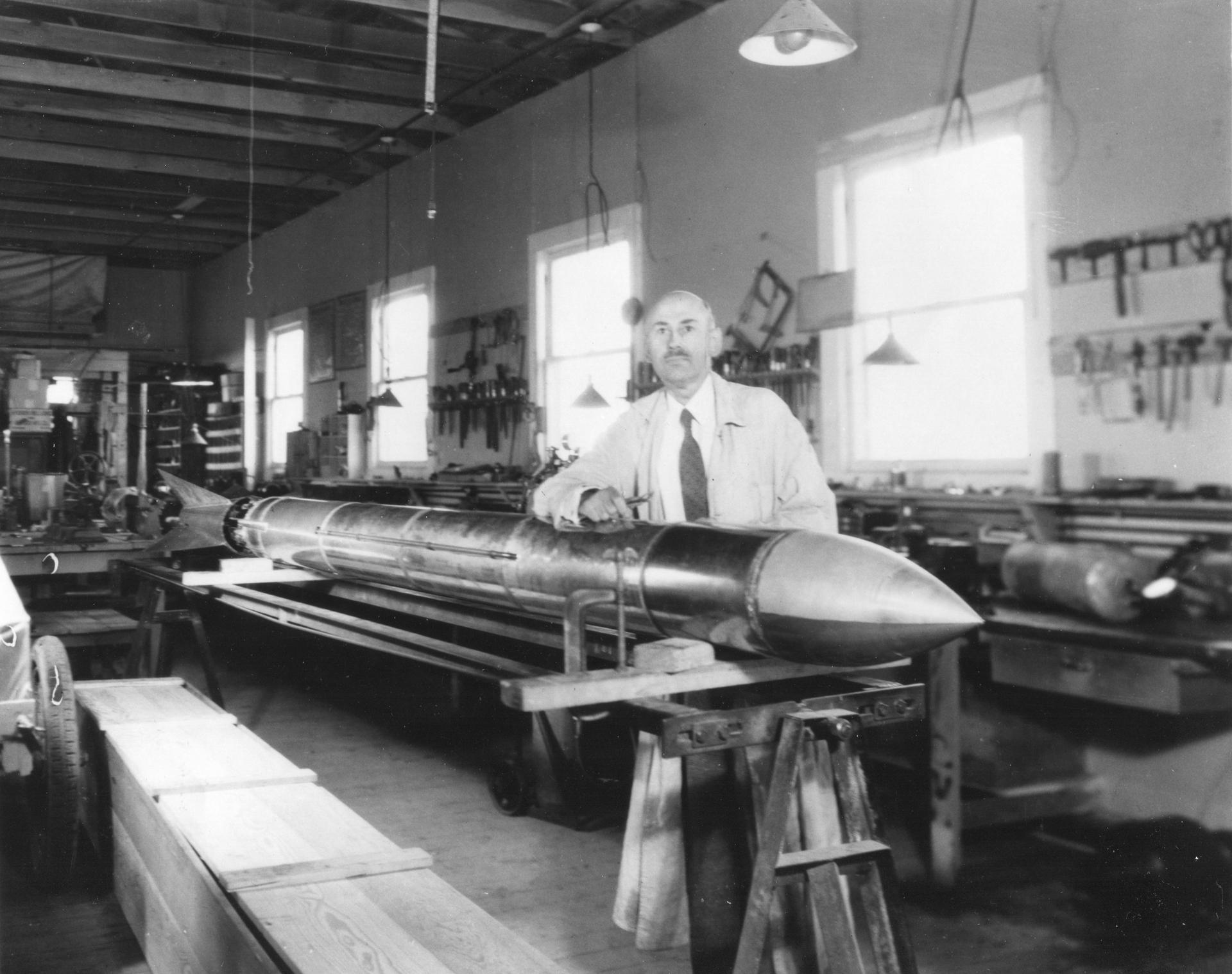 Dr. Robert Goddard stands next to his rocket in his workshop