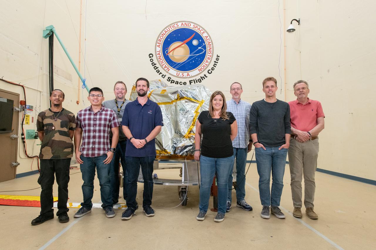 The Goddard Space Flight Center (GSFC) environmental testing team poses with the bagged Ocean Color Instrument (OCI) behind them in the acoustic chamber prior to testing. The acoustic testing will ensure that functionality of OCI is not impaired by severe launch environments.  OCI is a highly advanced optical spectrometer that will be used to measure properties of light over portions of the electromagnetic spectrum. It will enable continuous measurement of light at finer wavelength resolution than previous NASA satellite sensors, extending key system ocean color data records for climate studies. OCI is PACE's (Plankton, Aerosol, Cloud, ocean Ecosystem) primary sensor built at Goddard Space Flight Center in Greenbelt, MD.